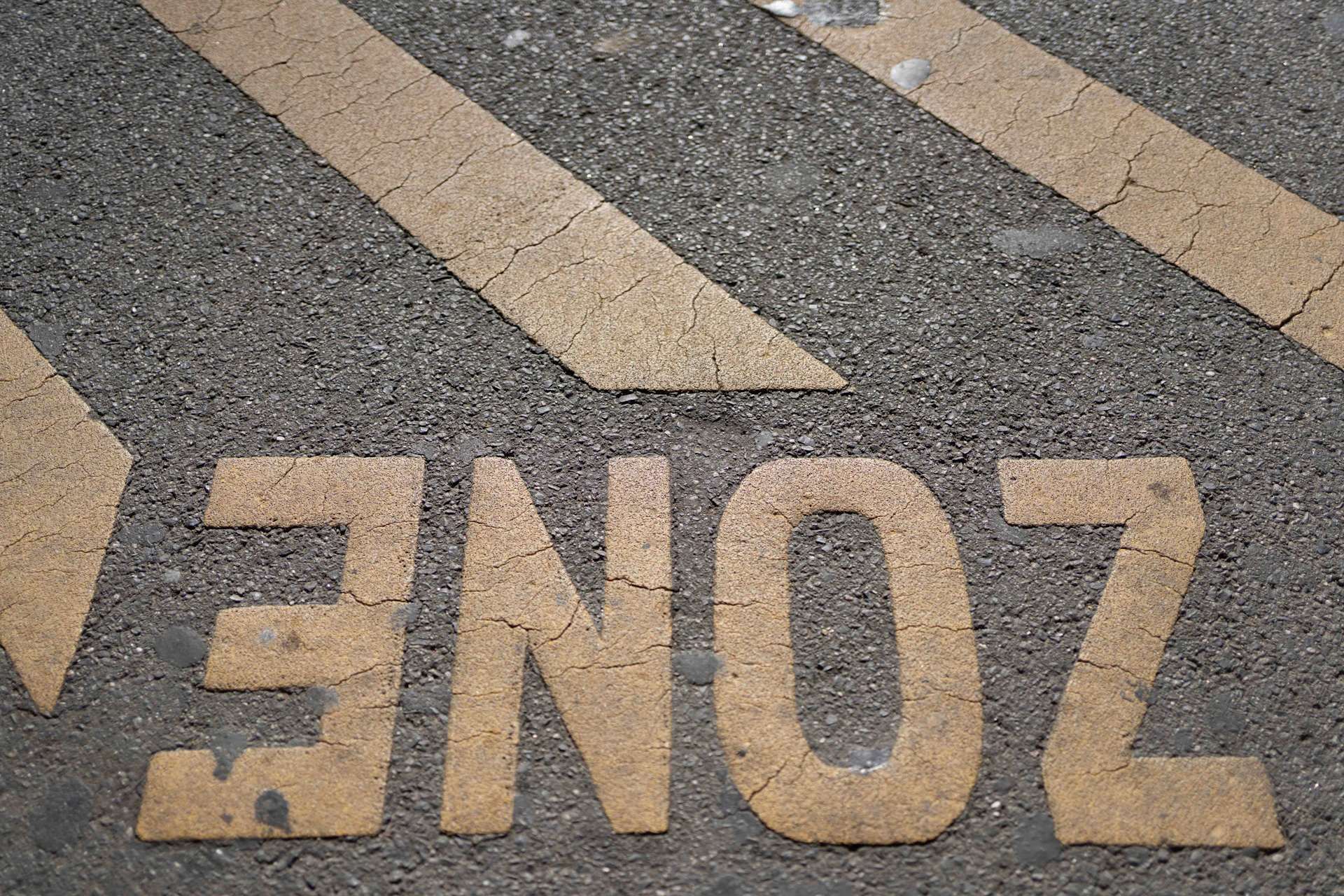 Yellow zone text and stripes painted on grey asphalt.