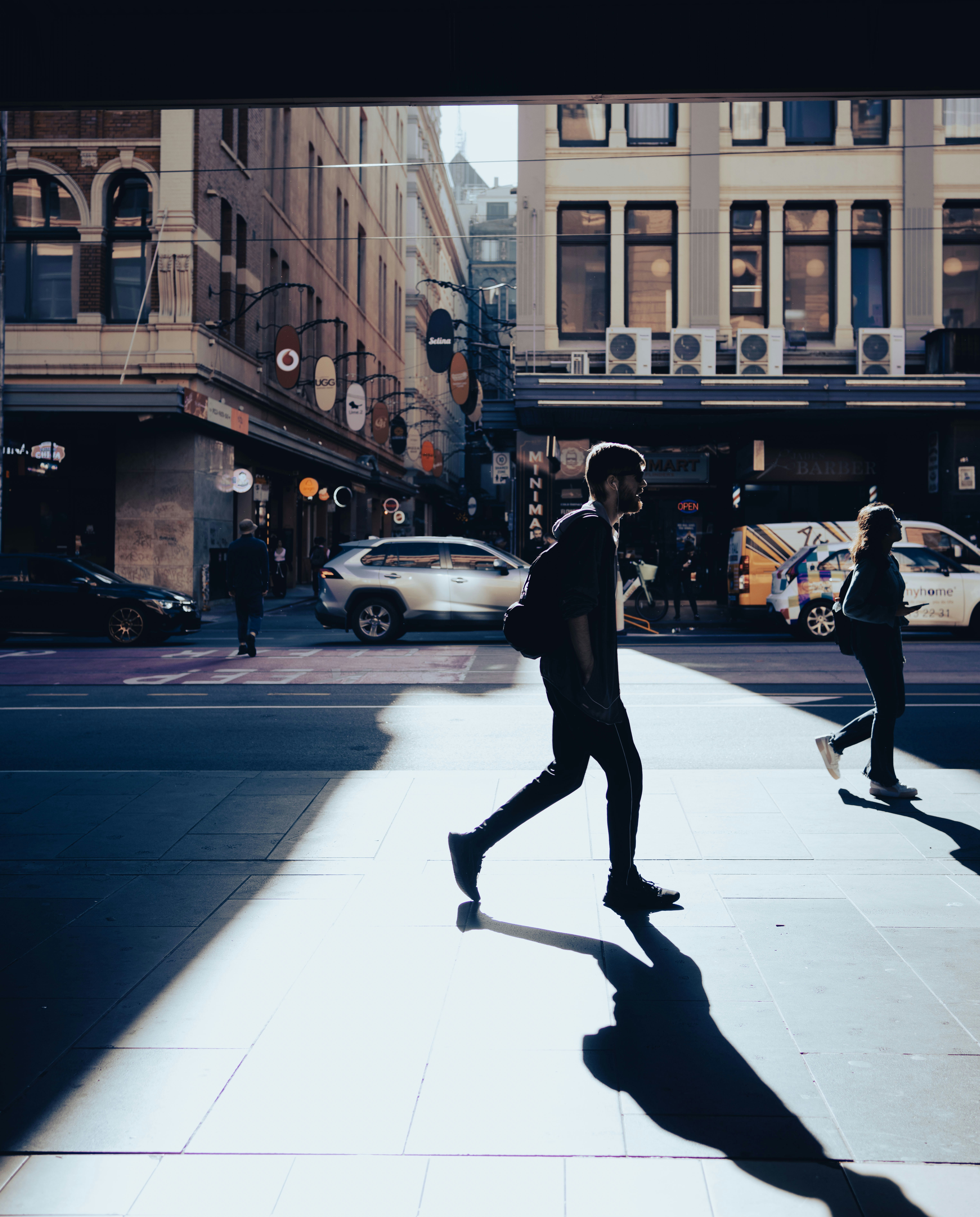 Silhouetted pedestrians cross a sunlit urban street.