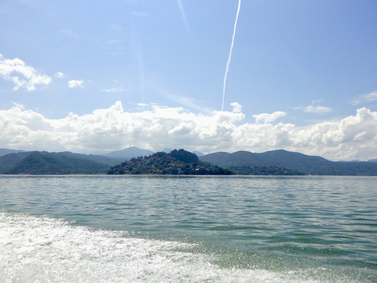 Le lac de Valle de Bravo vu depuis un bateau, avec des collines boisées et des maisons sur la rive