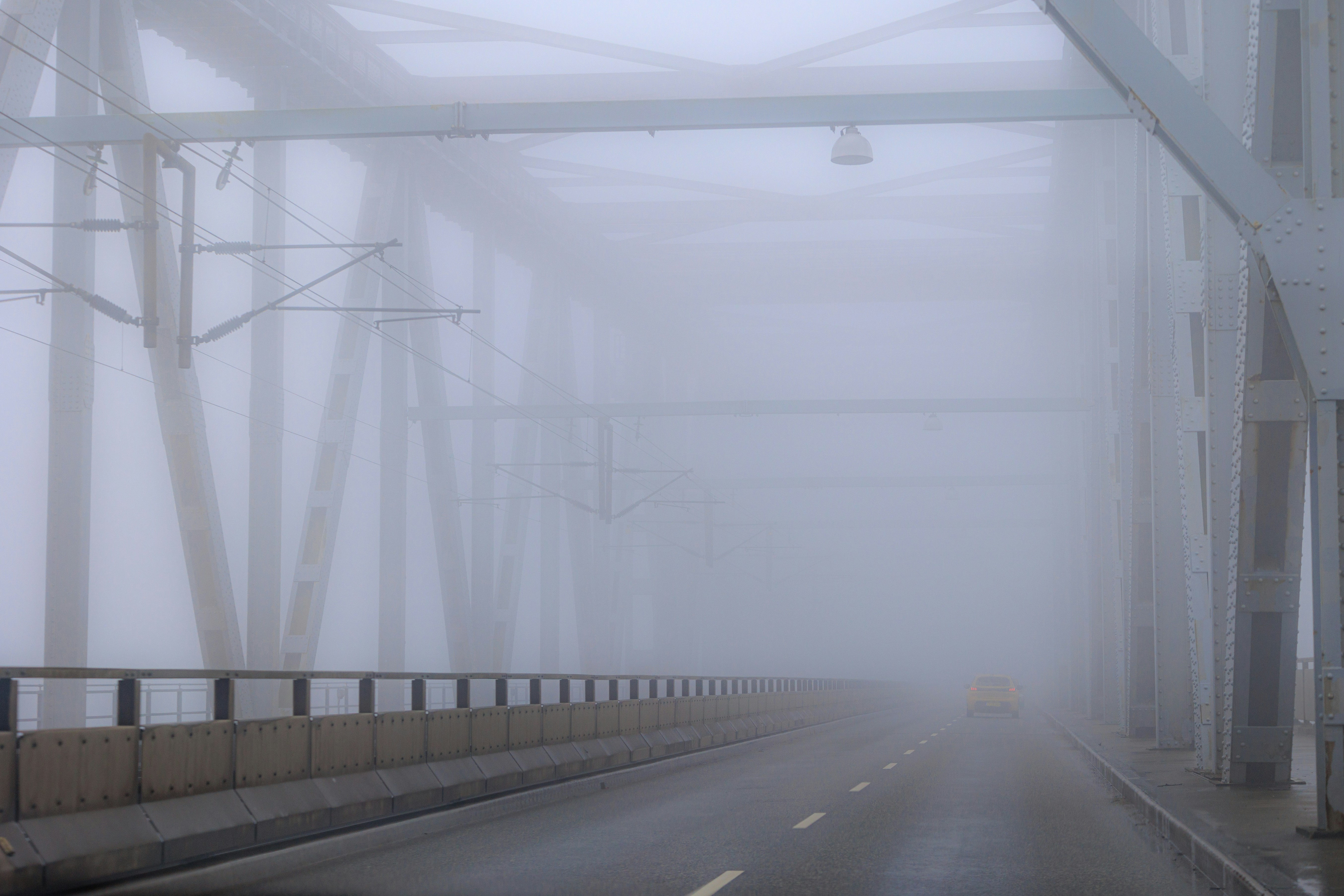 Dense fog obscures a bridge and wet road ahead.