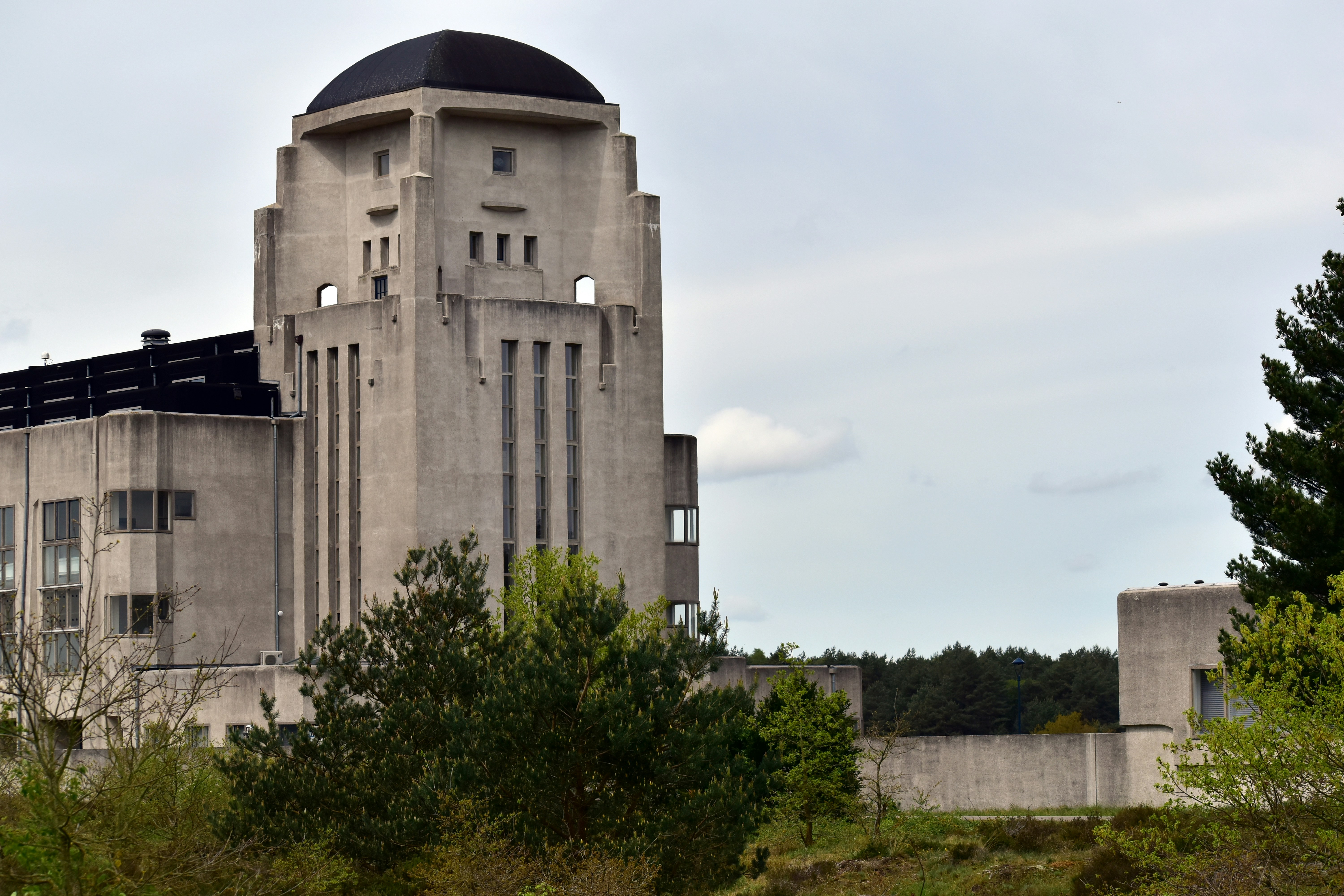 Edifício histórico de concreto com telhado em cúpula e árvores ao redor.