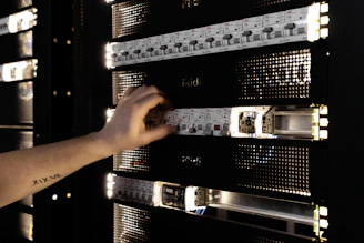 A hand adjusting components in a glowing server rack.
