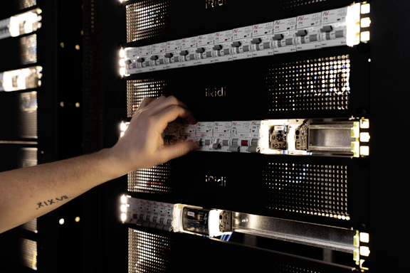 A hand adjusting components in a glowing server rack.