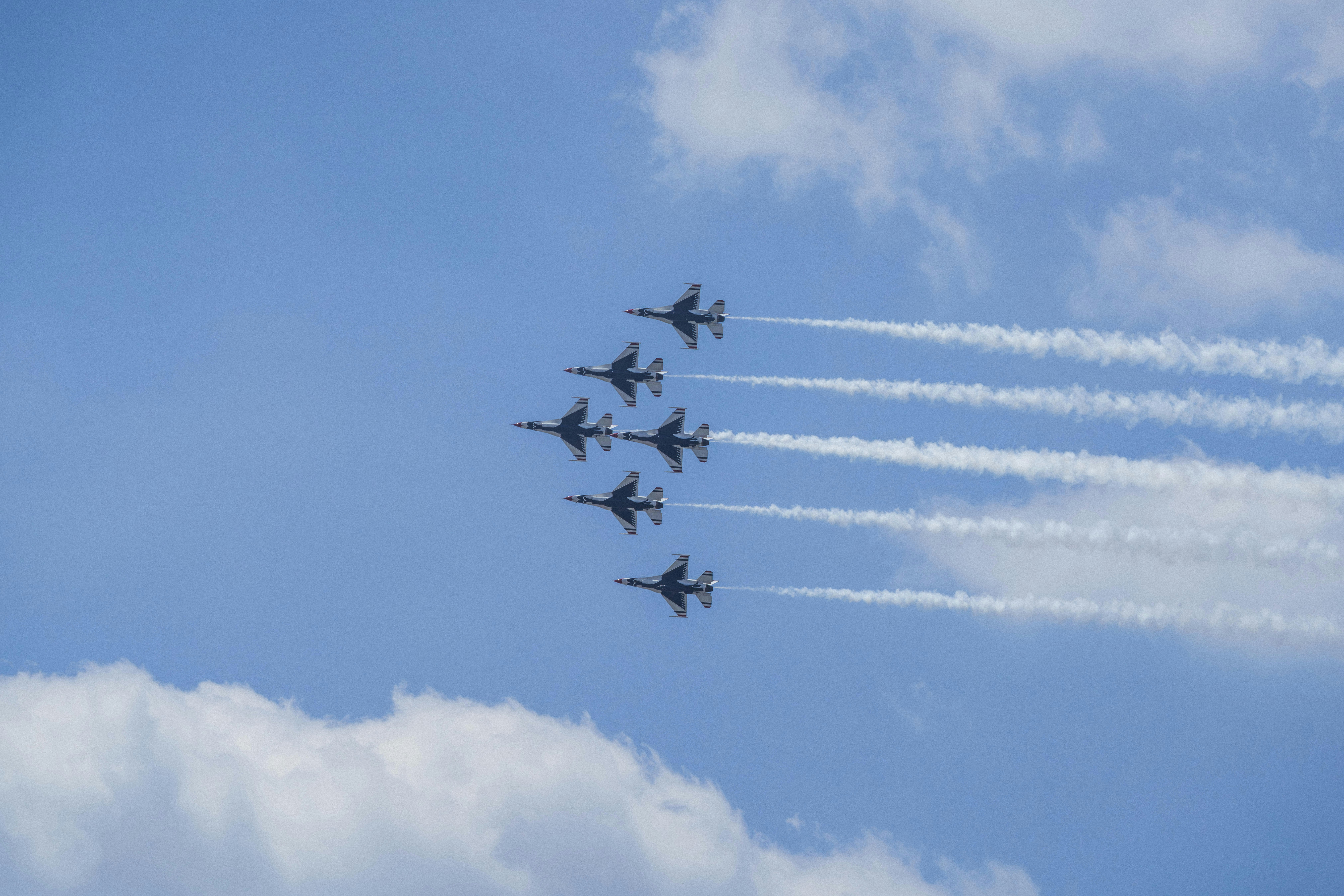 Jets flying in formation leaving contrails against a blue sky.
