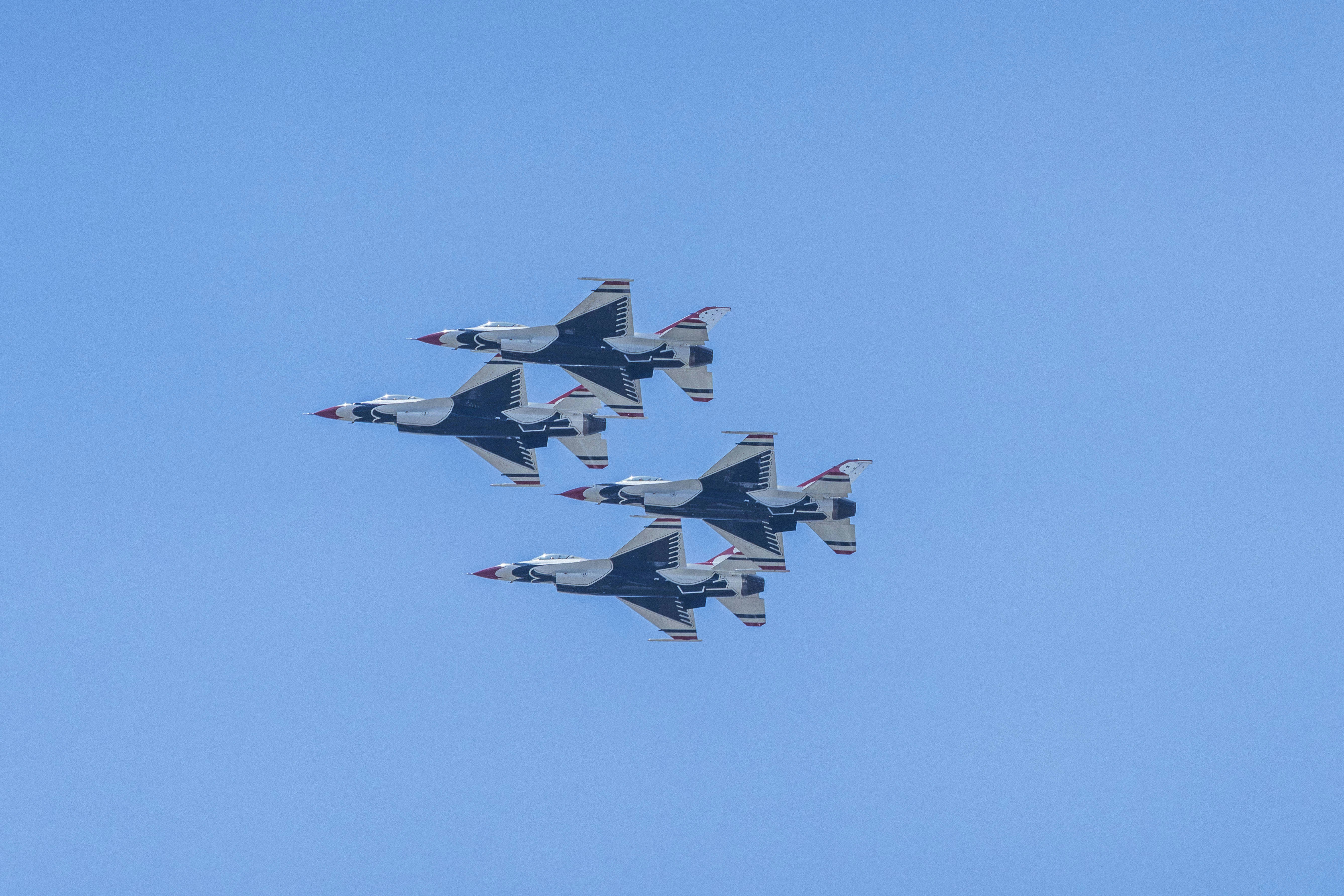 Four fighter jets flying in formation in a blue sky.