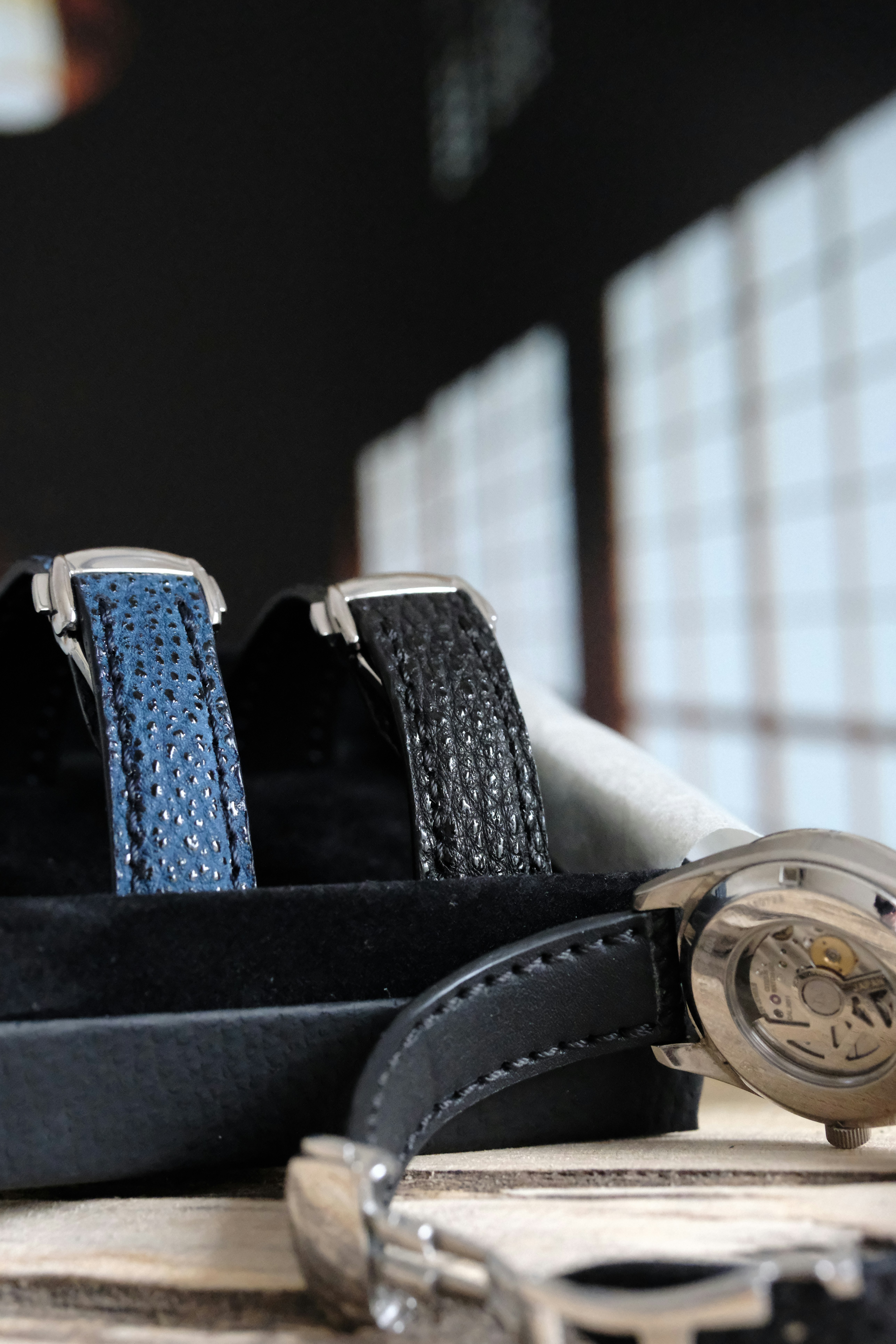 Blue and black watch straps with a watch on wood.