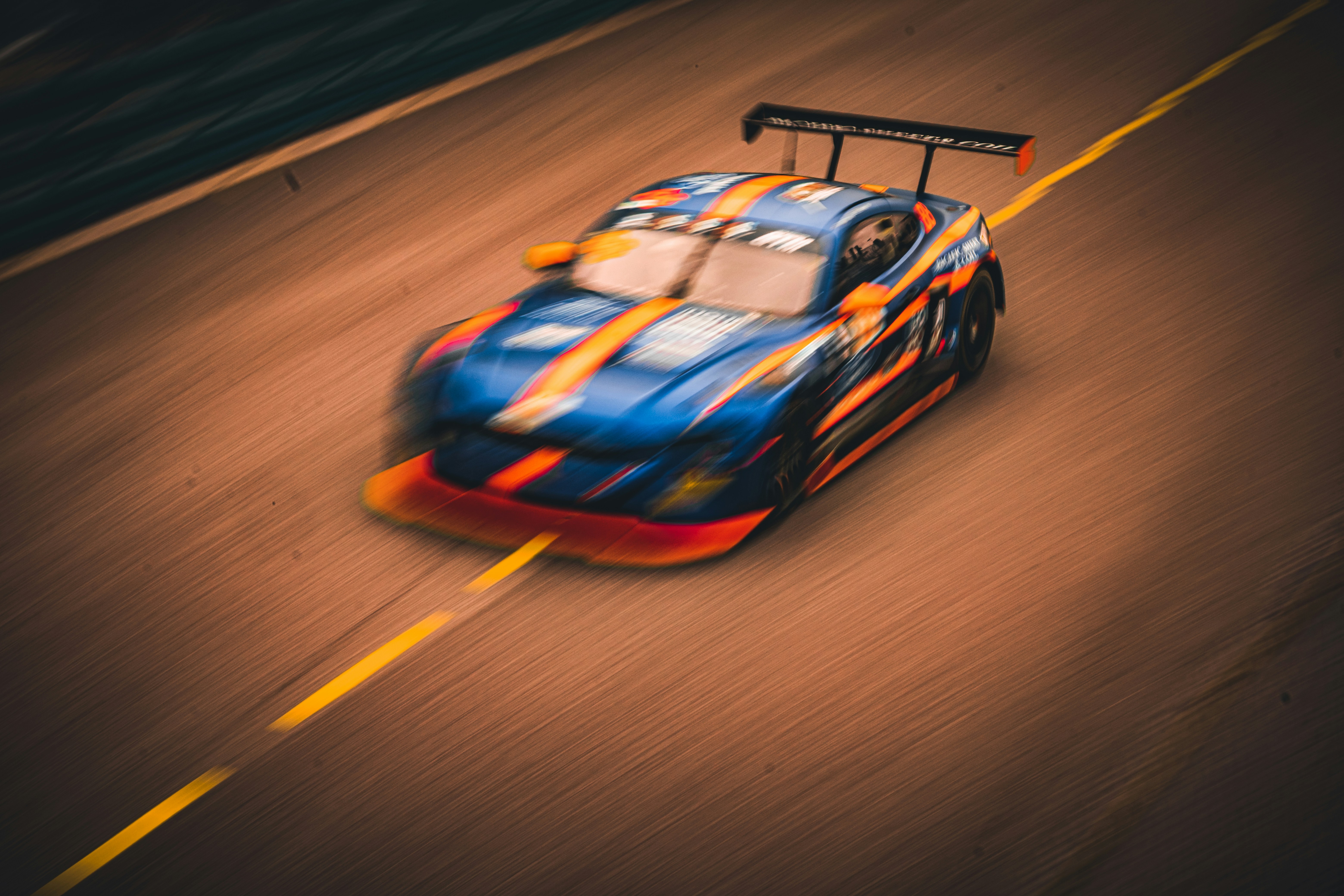 Cars High Angle Artistic Panning Photograph Capturing A Blue And Orange Ford Mustang Gt Race Car Speeding Down A Track With Dramatic Motion Blur. The Extreme Velocity Effect Accentuates The Car’s Aggressive Lines, Massive Rear Wing, And Aerodynamic Body K