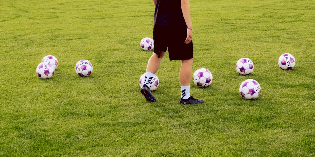 Person on a grassy field surrounded by multiple soccer balls.