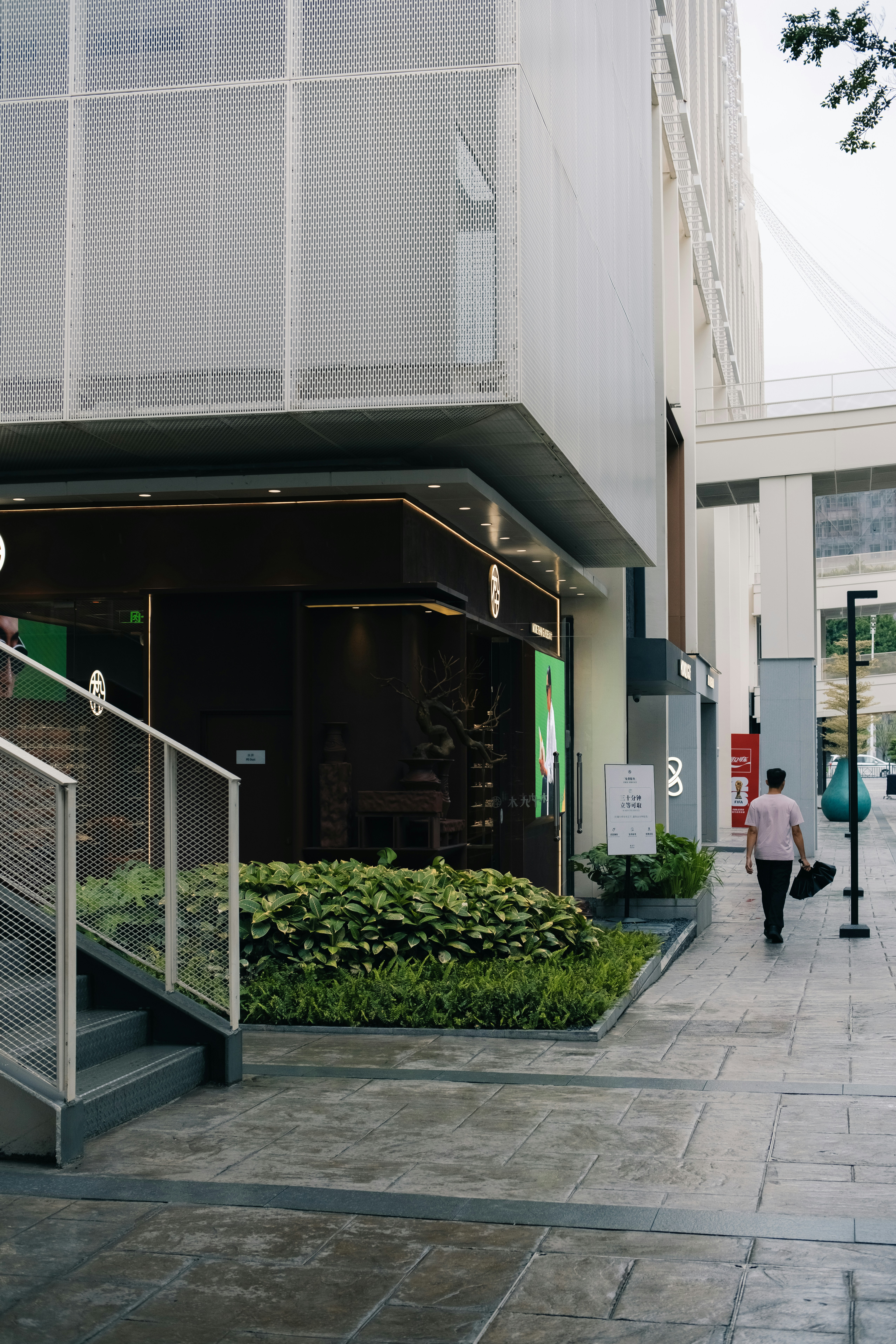 Modern building exterior with green plants and a man walking.