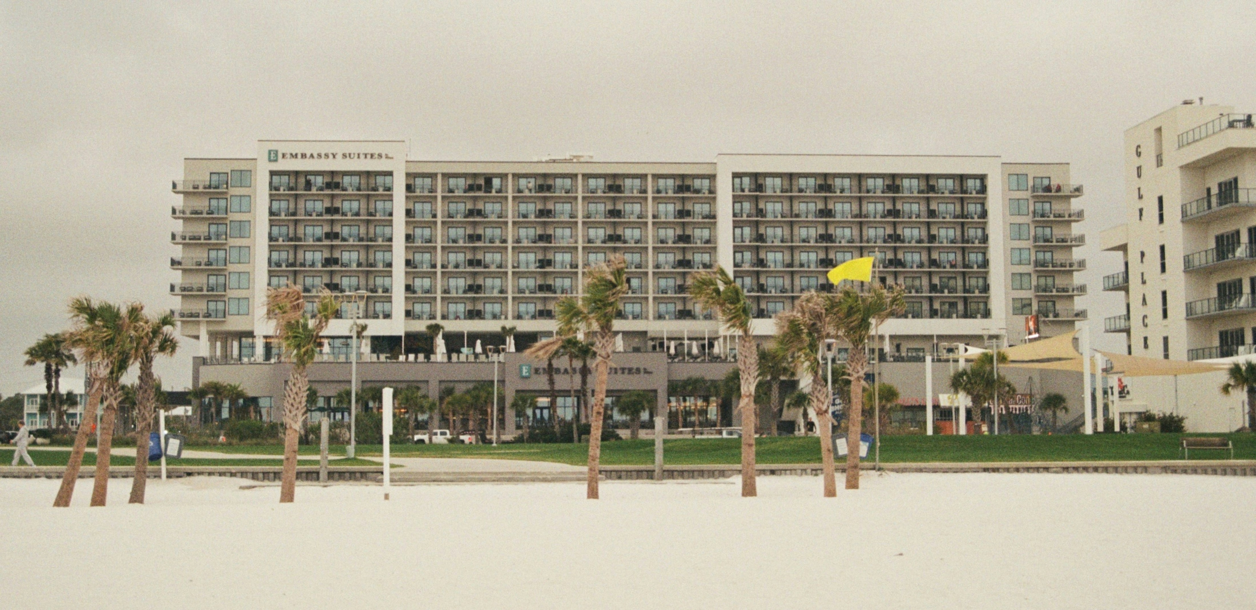 Hotel building with palm trees on a sandy beach.