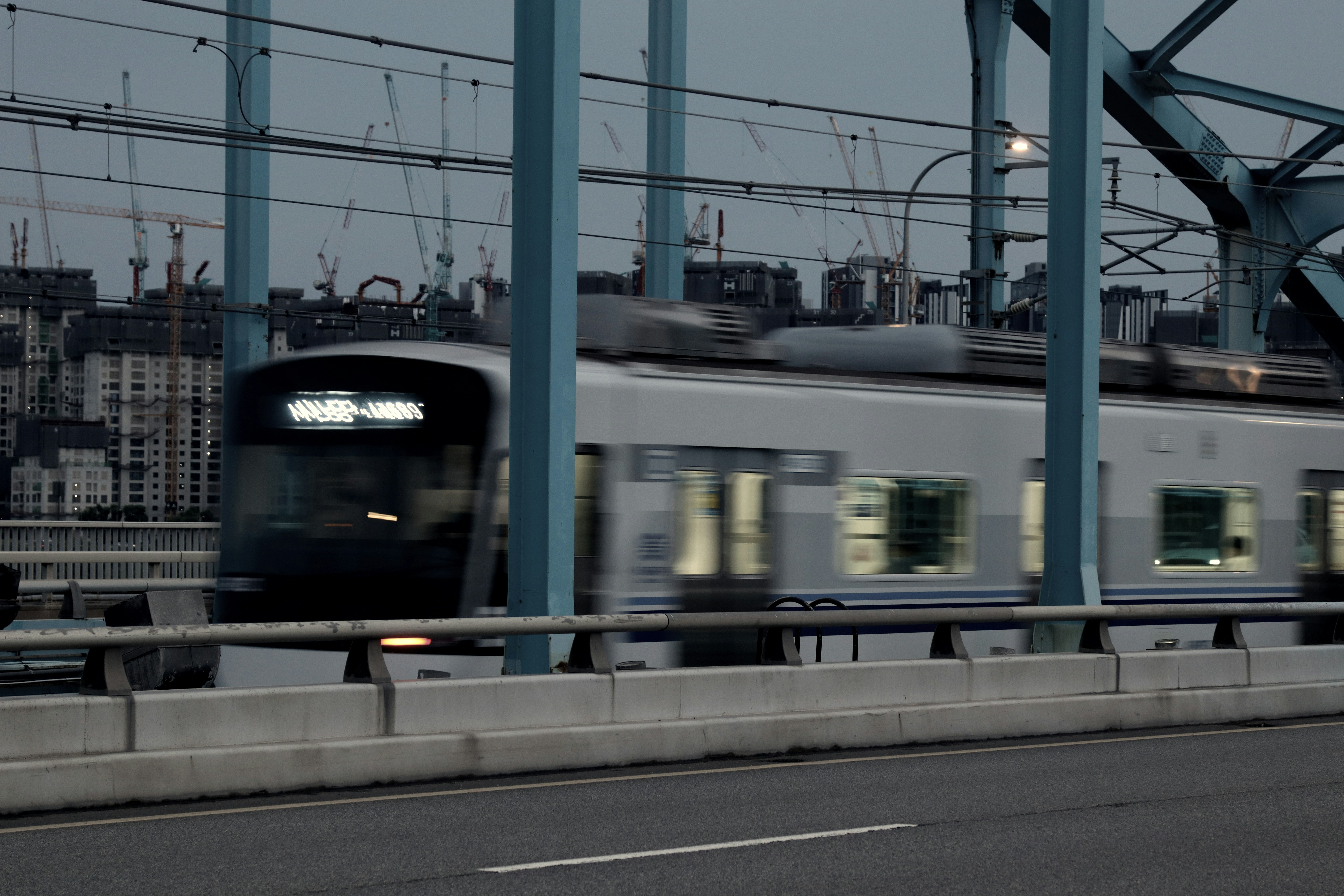 Fast-moving train crossing a blue bridge with city lights.