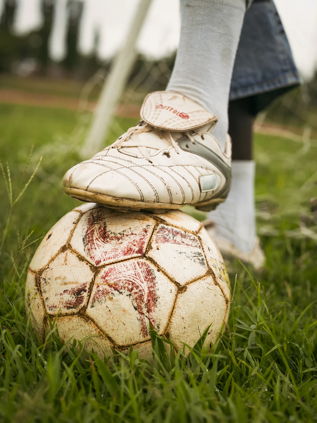 A child's foot in a football boot resting on a worn ball