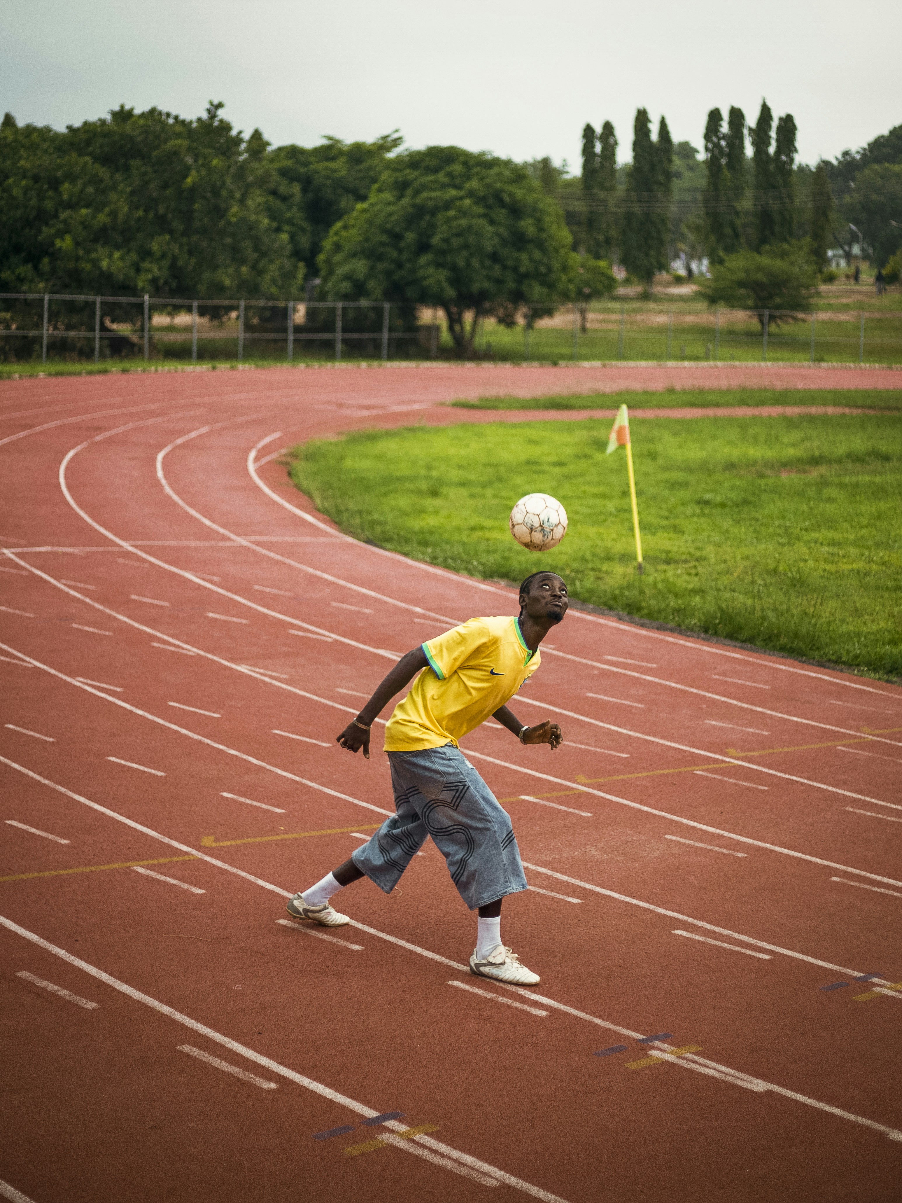 Man juggling soccer ball on head on red running track