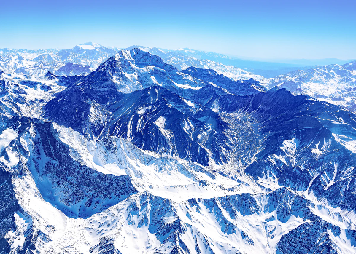Aerial view from a plane over the snow-covered high Andes around Aconcagua, ridges and glaciated valleys stretching to the horizon under a clear blue sky.