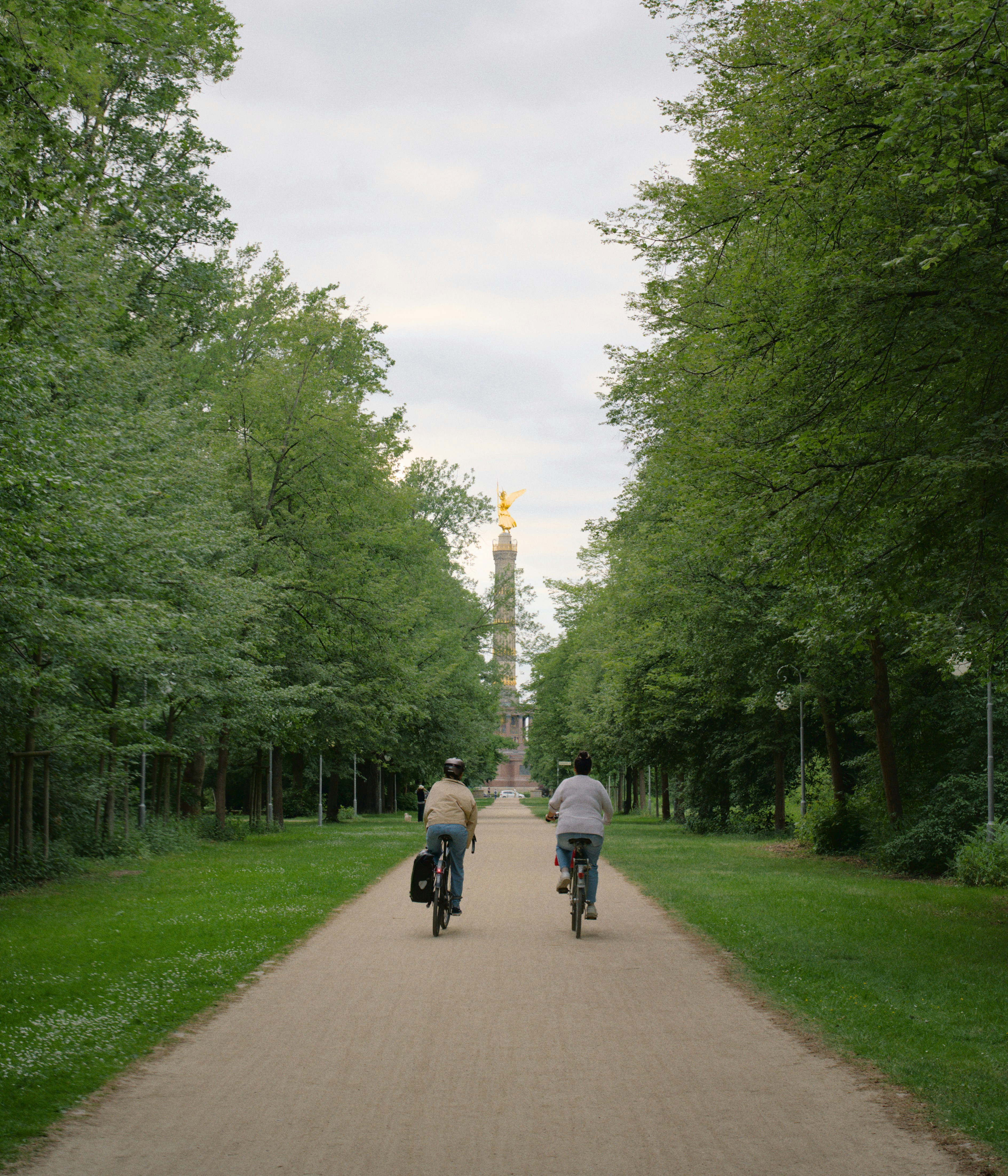 Due ciclisti su un sentiero alberato verso un monumento lontano.