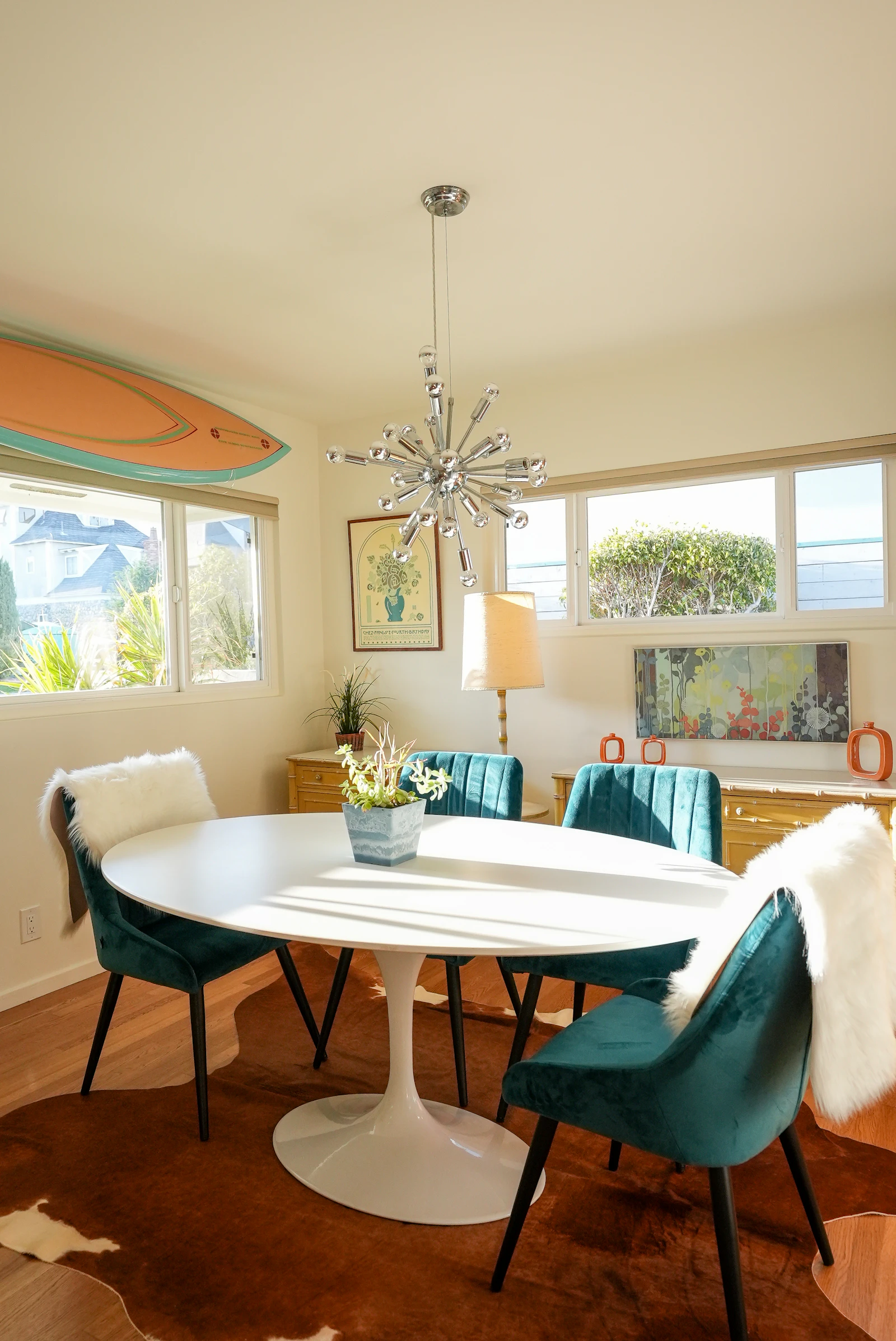 Dining room with an oval table, teal chairs and a surfboard
