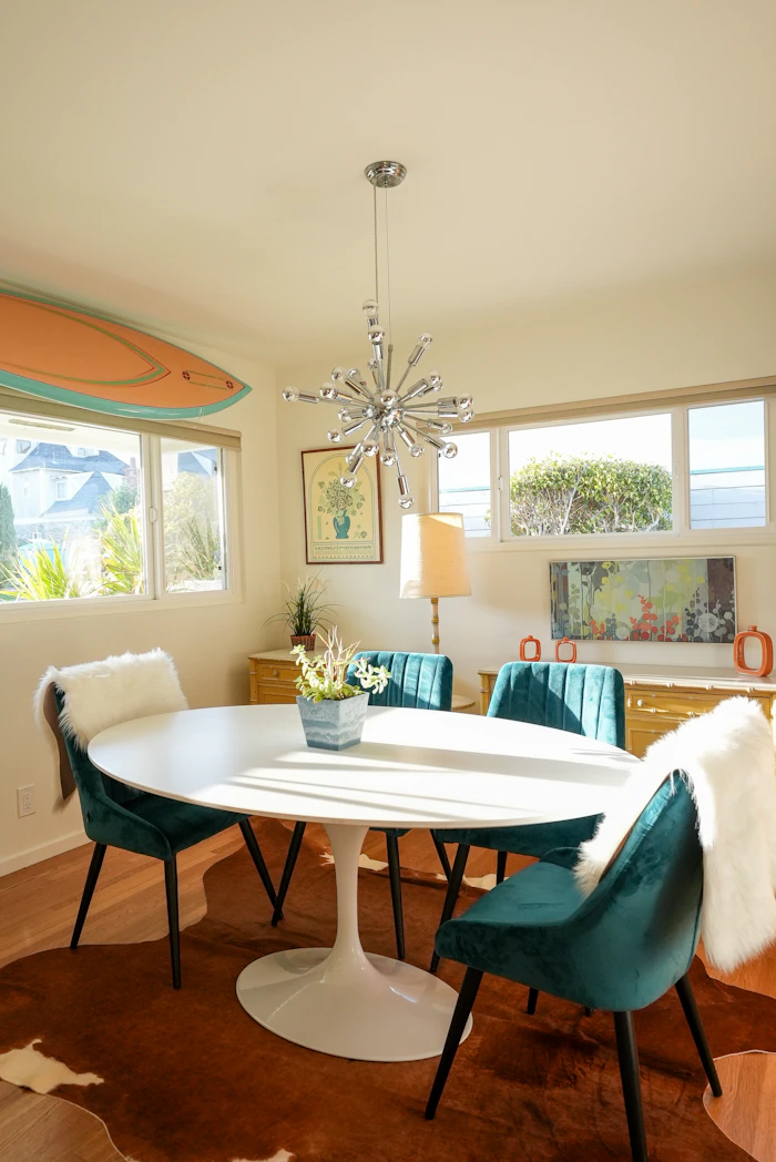 Dining room with an oval table, teal chairs and a surfboard