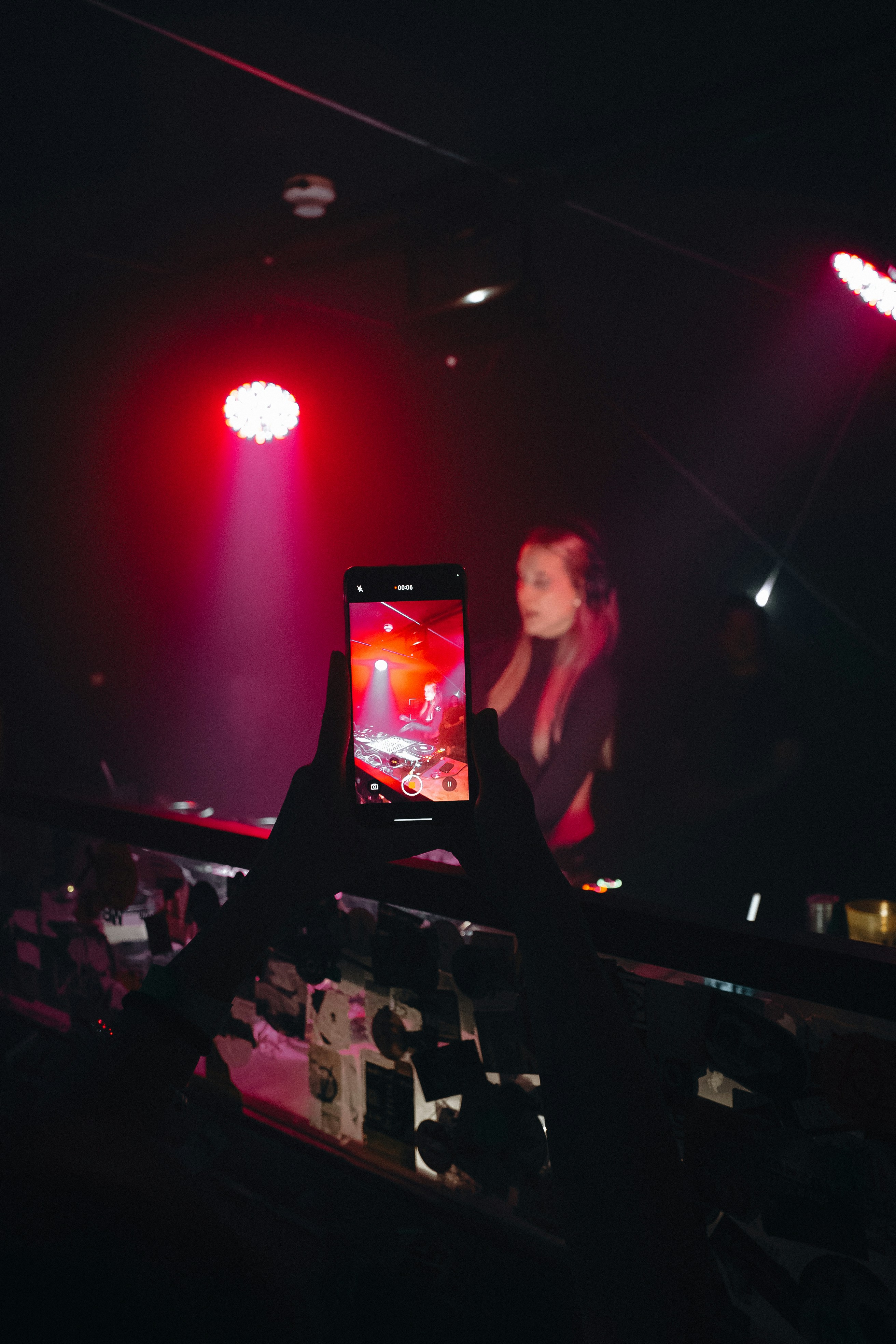 Hands holding a phone recording a dj at a concert