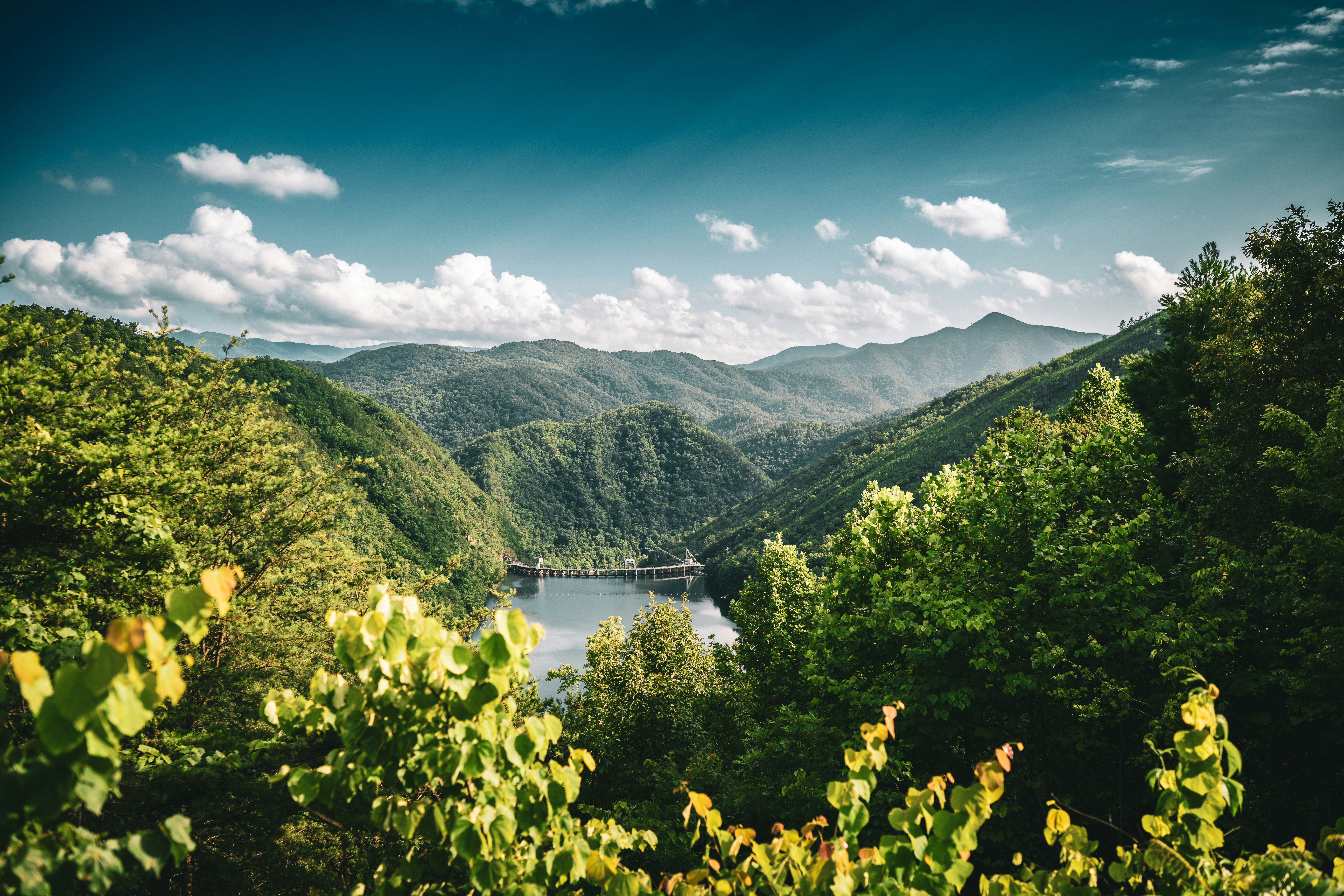 Serene lake nestled among lush green mountains under blue sky.