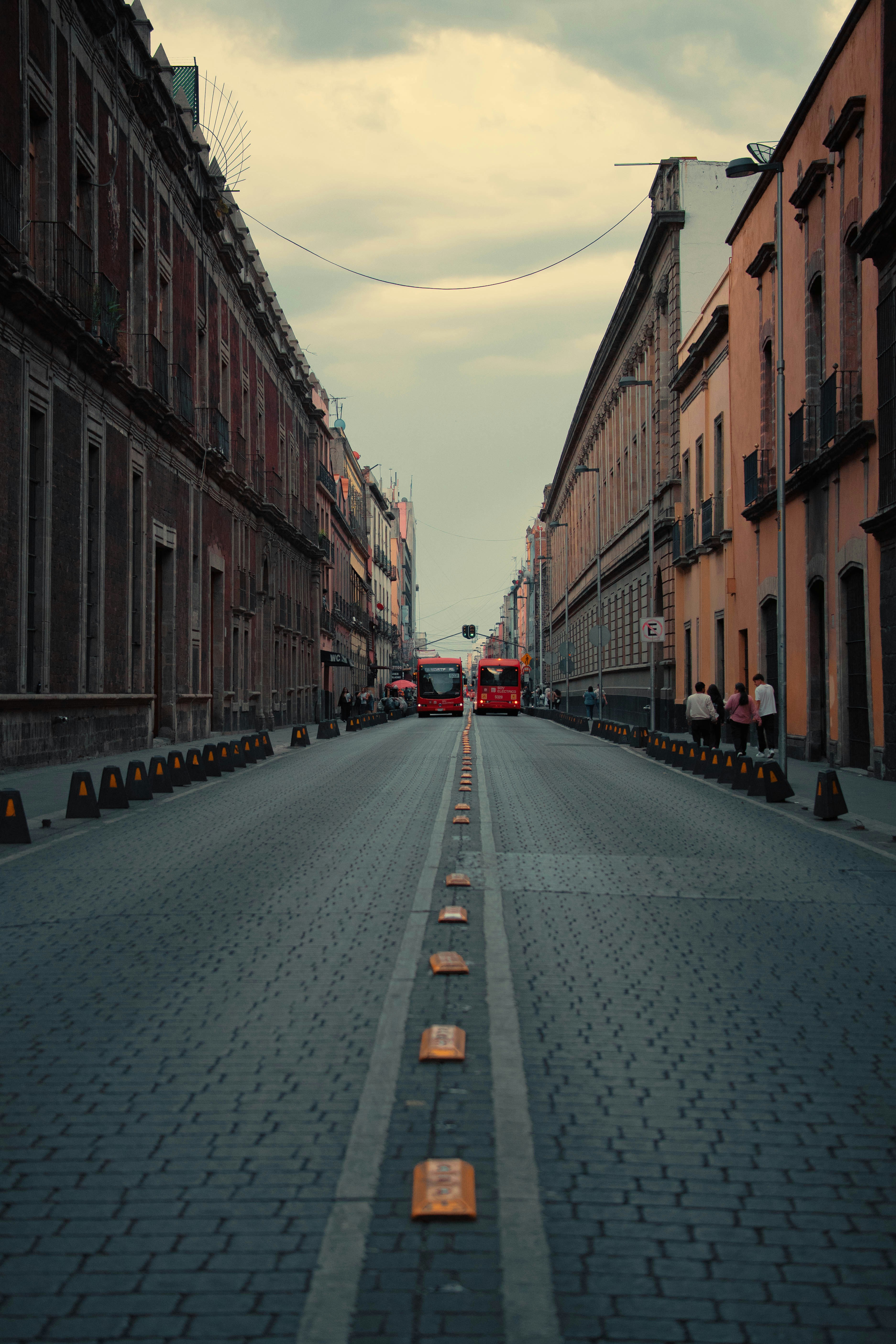 Cobblestone street lined with buildings and distant red buses.