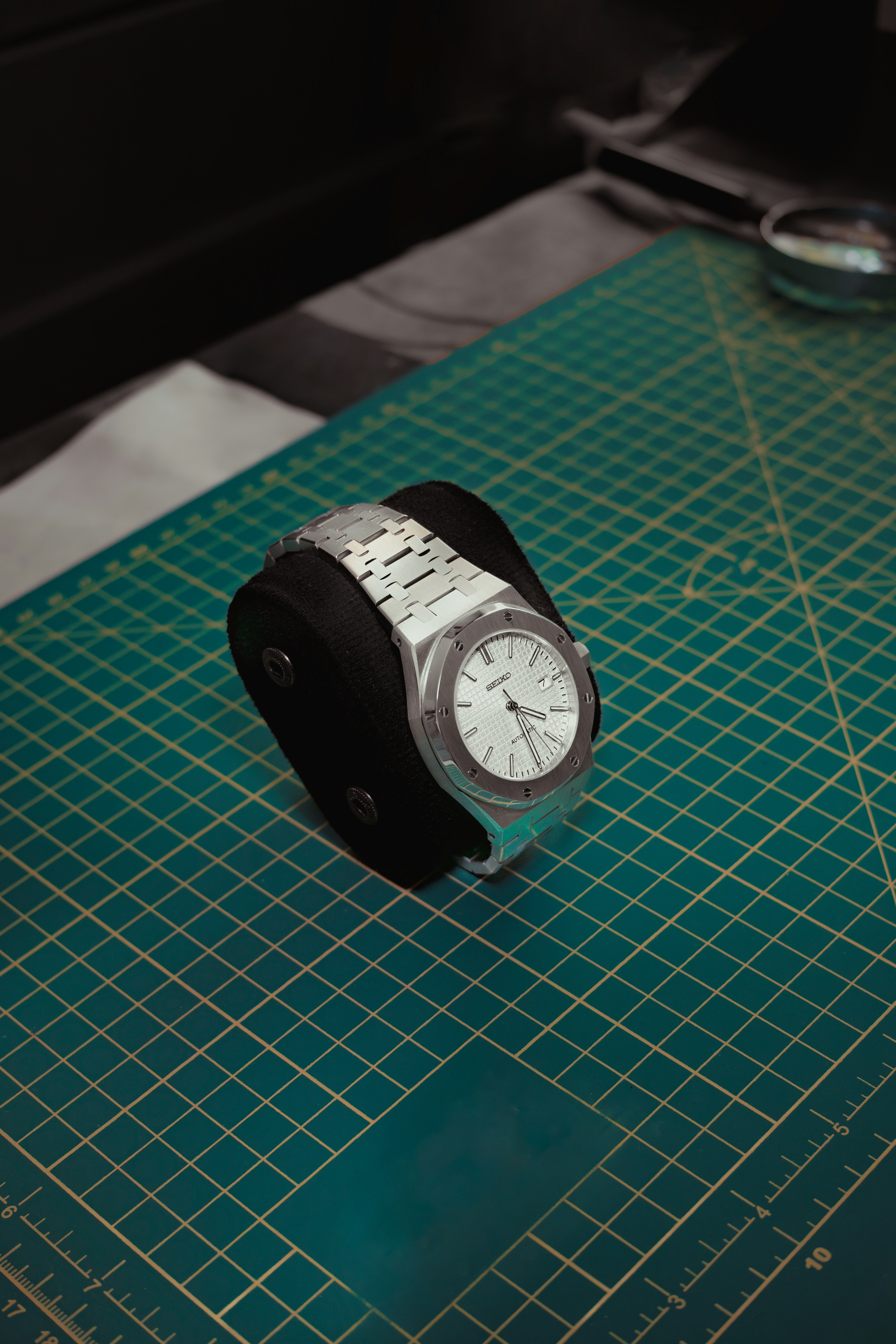 Silver watch on a black stand on a green mat.