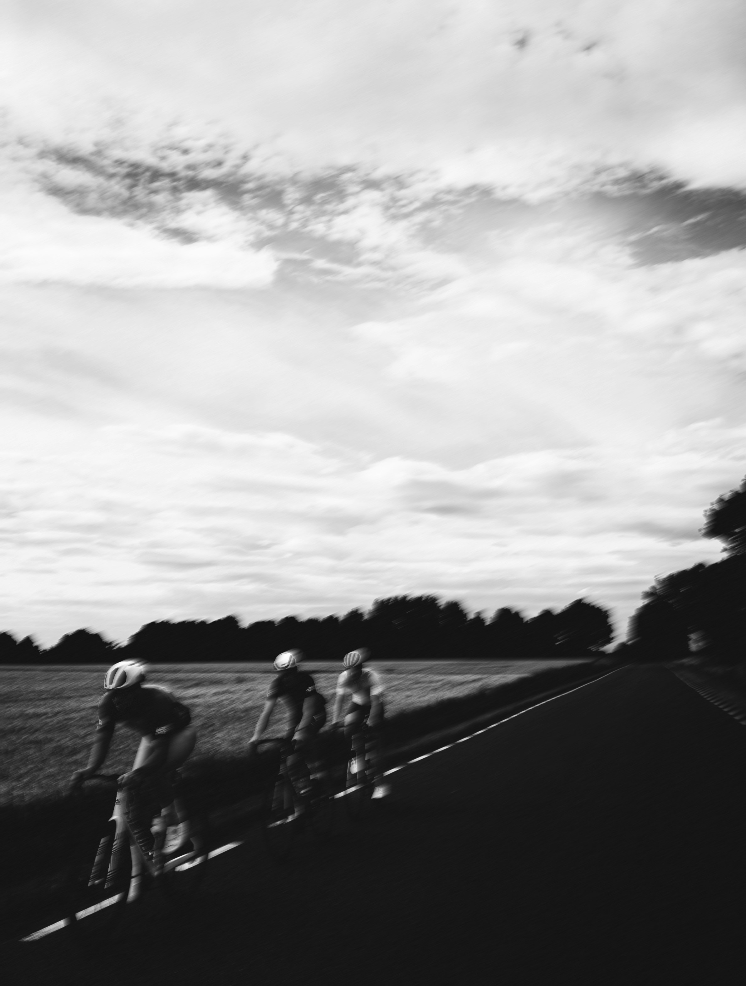 Motion-blurred cyclists racing on a rural road under cloudy sky.