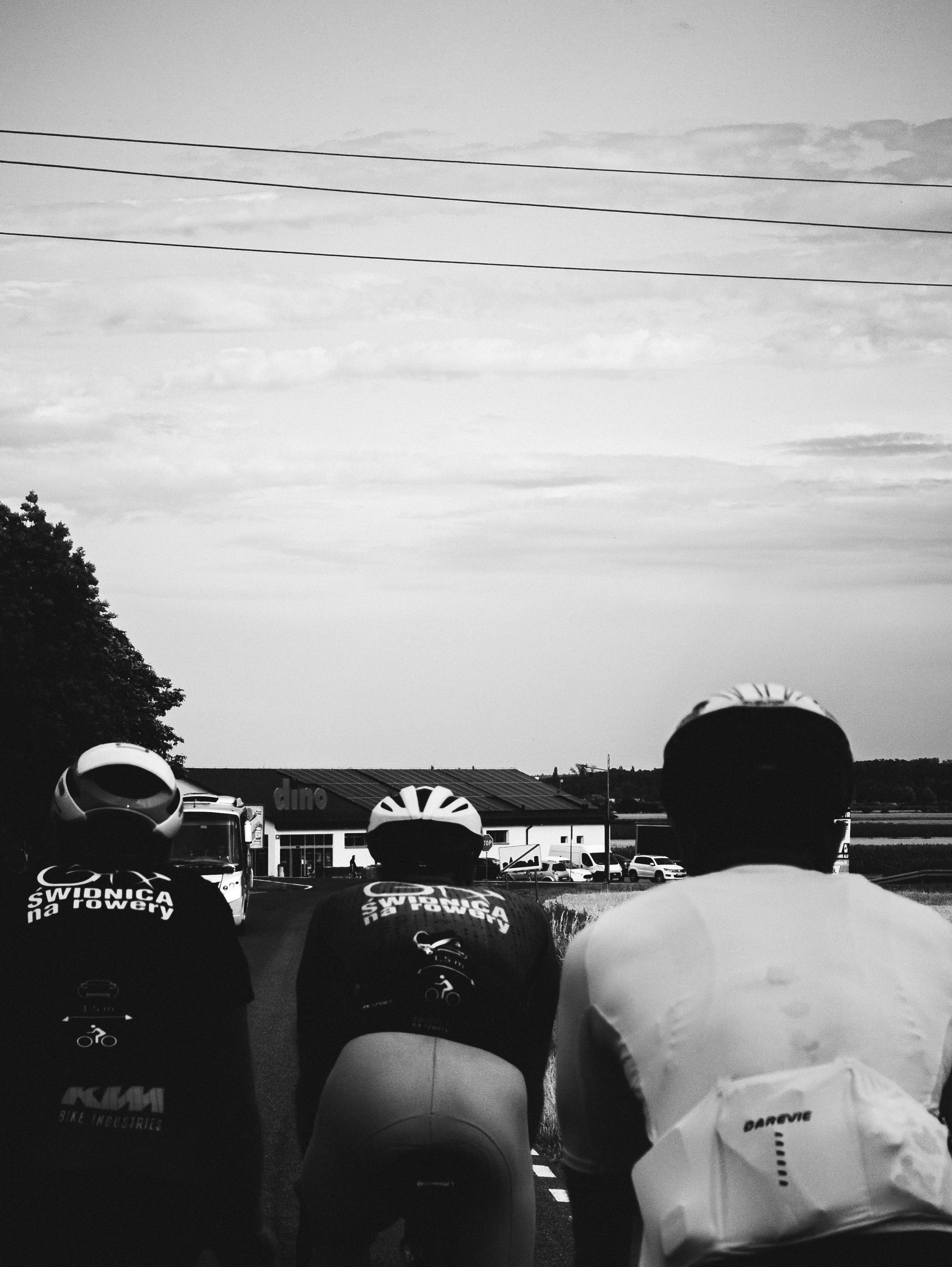Three riders in helmets from behind under a cloudy sky.