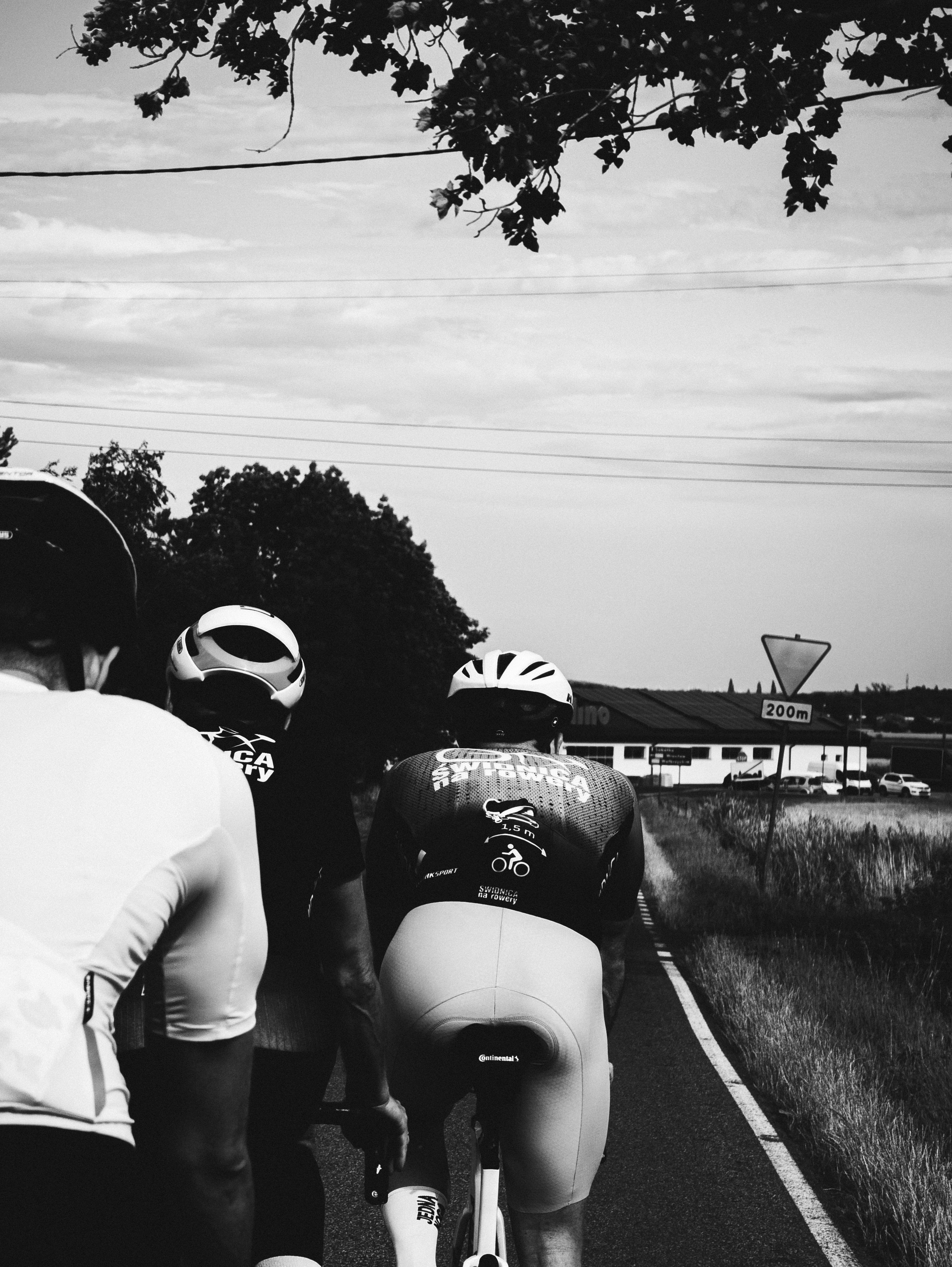 Cyclists ride on a rural road in black and white.