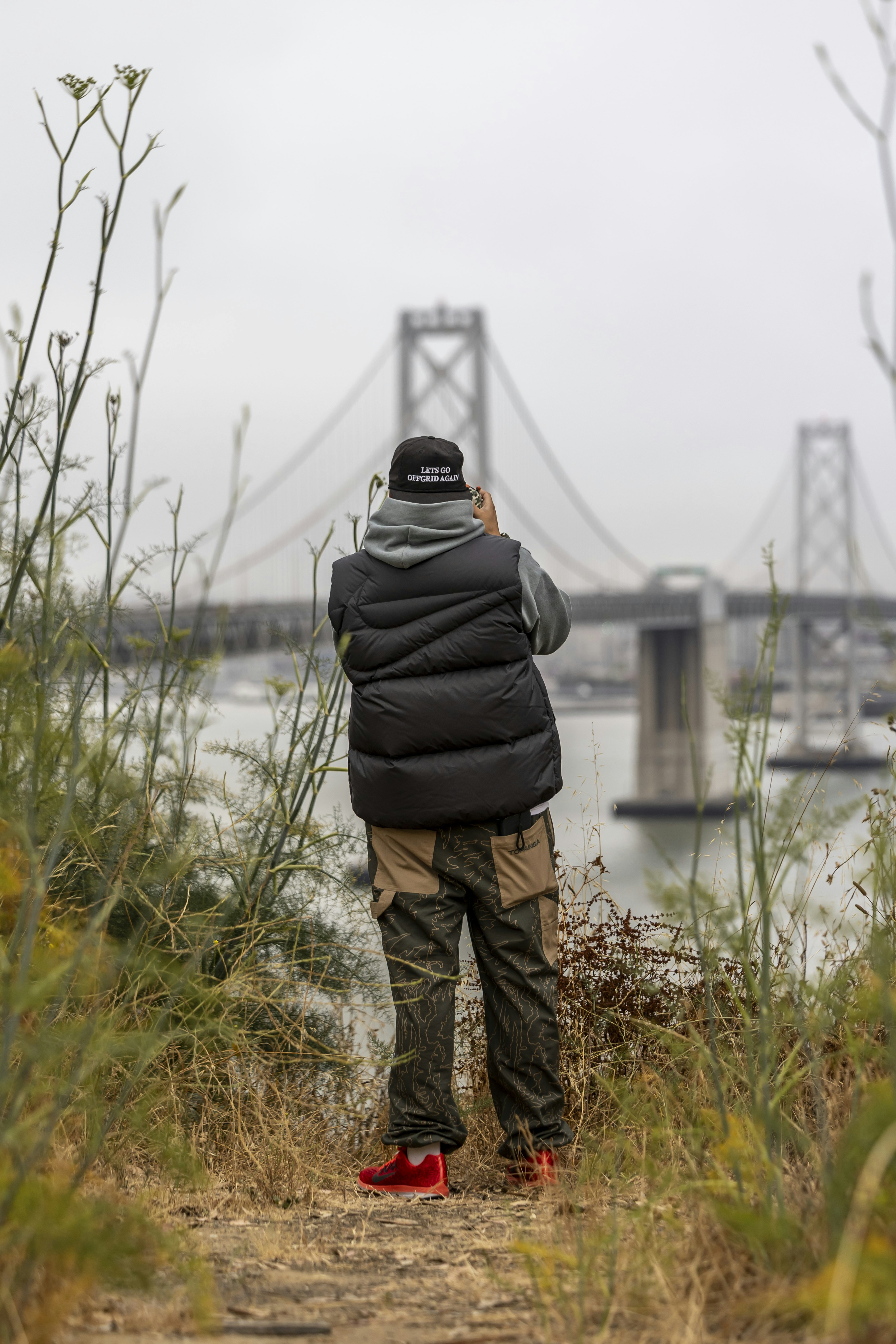 Man photographing a large suspension bridge on an overcast day.