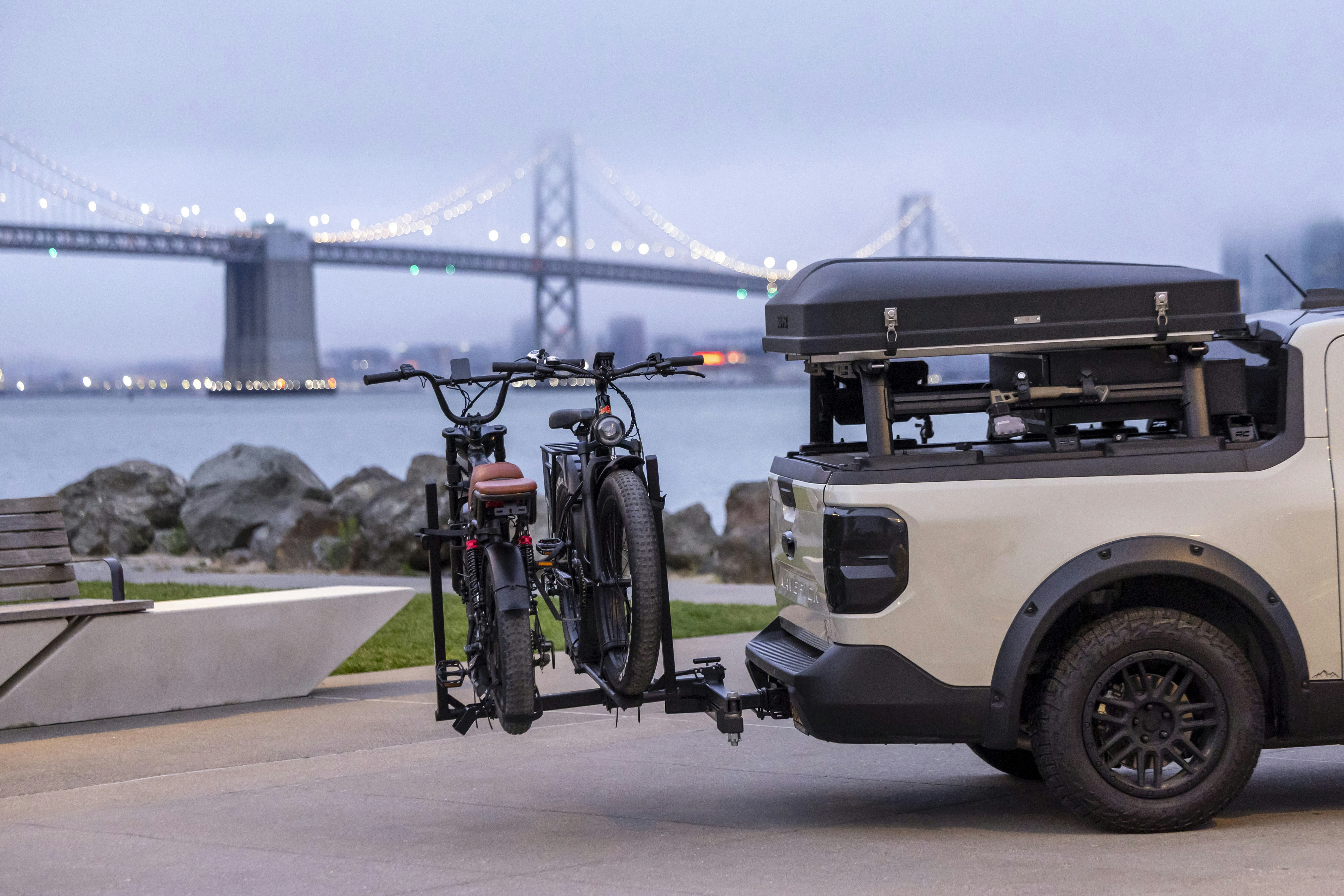 Pickup truck with bikes and tent by a bridge.