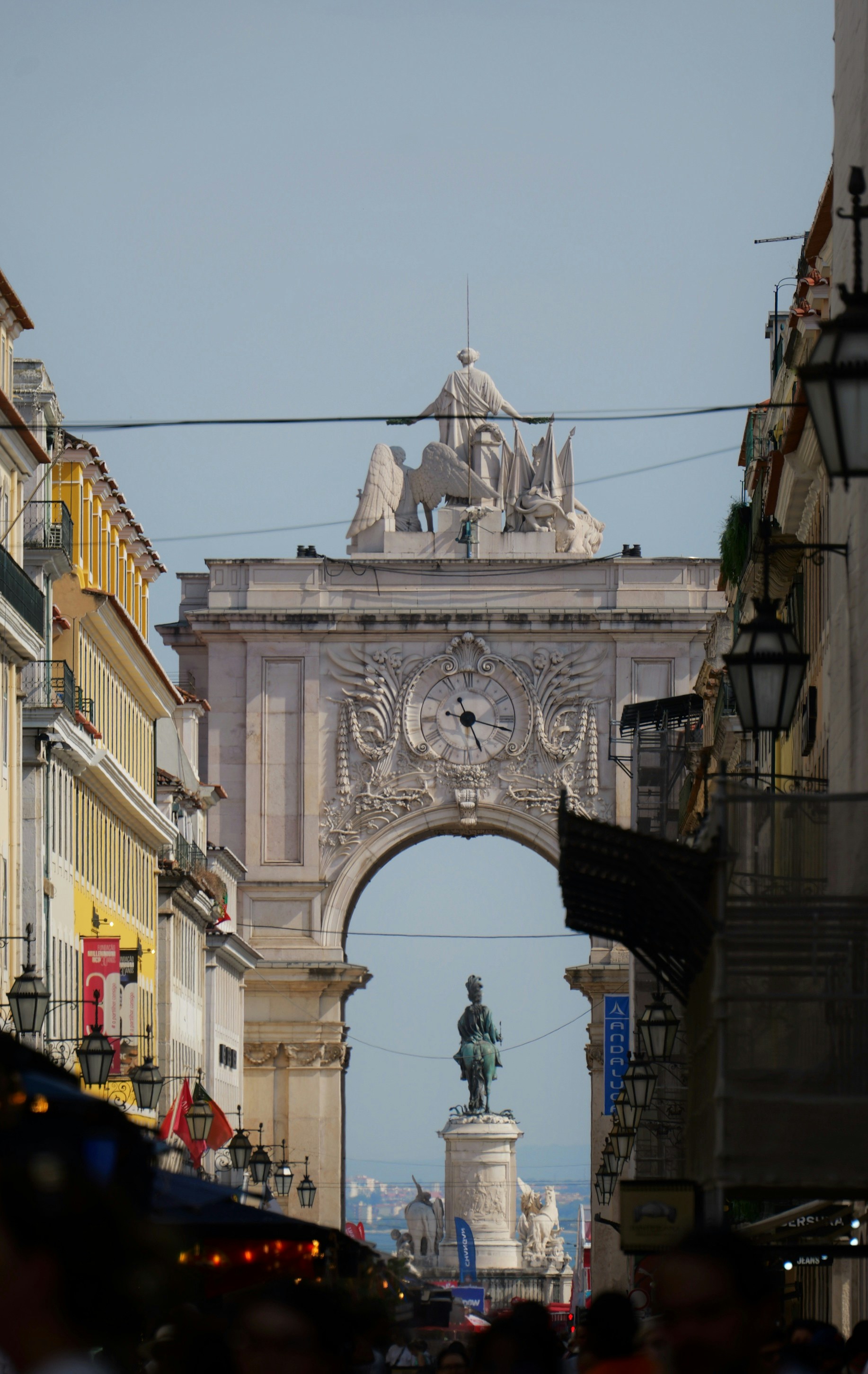 Street view of a grand archway and distant equestrian statue.
