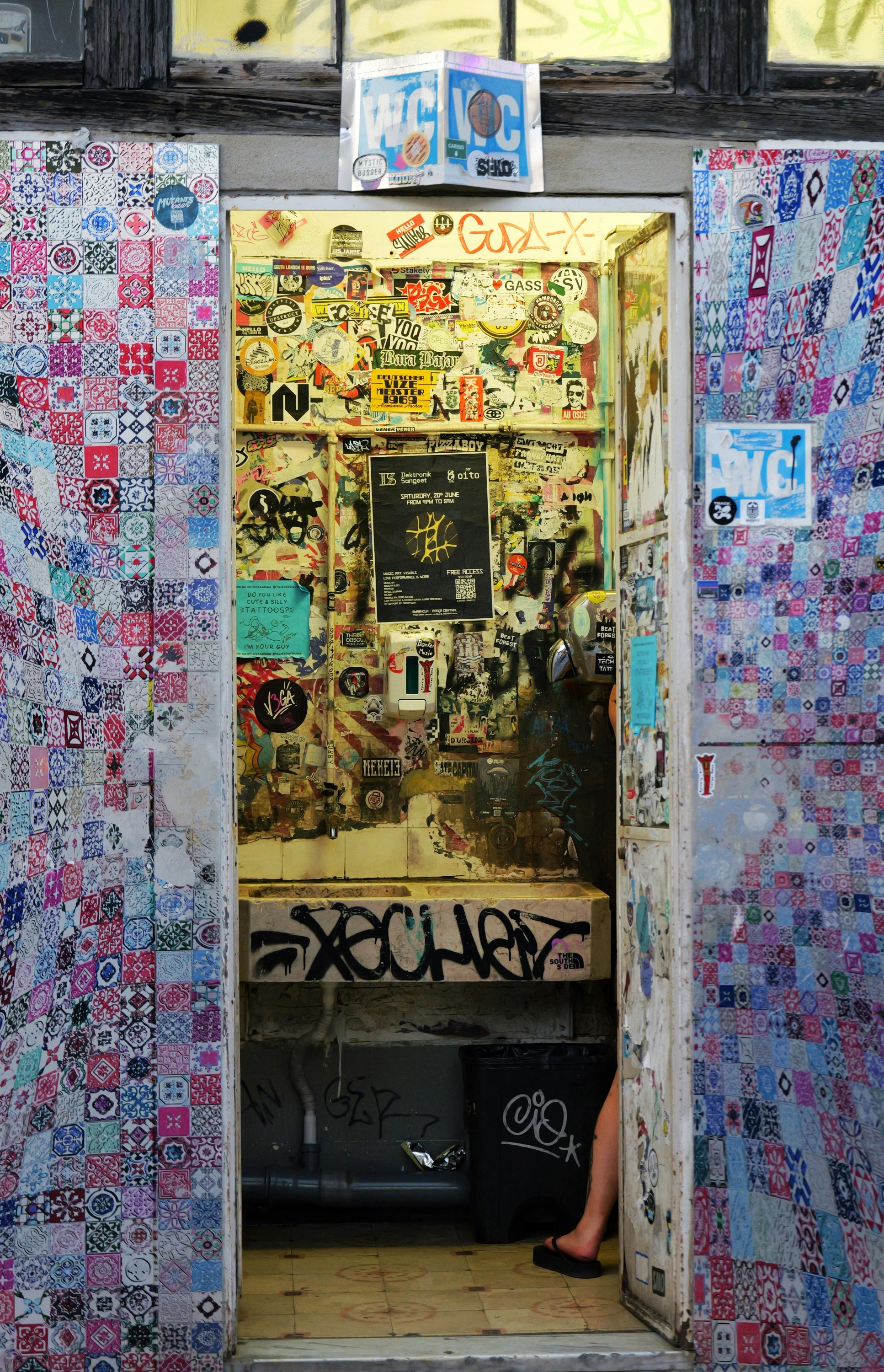 Colorful tiled entrance to a sticker-covered, graffiti-filled urban room.