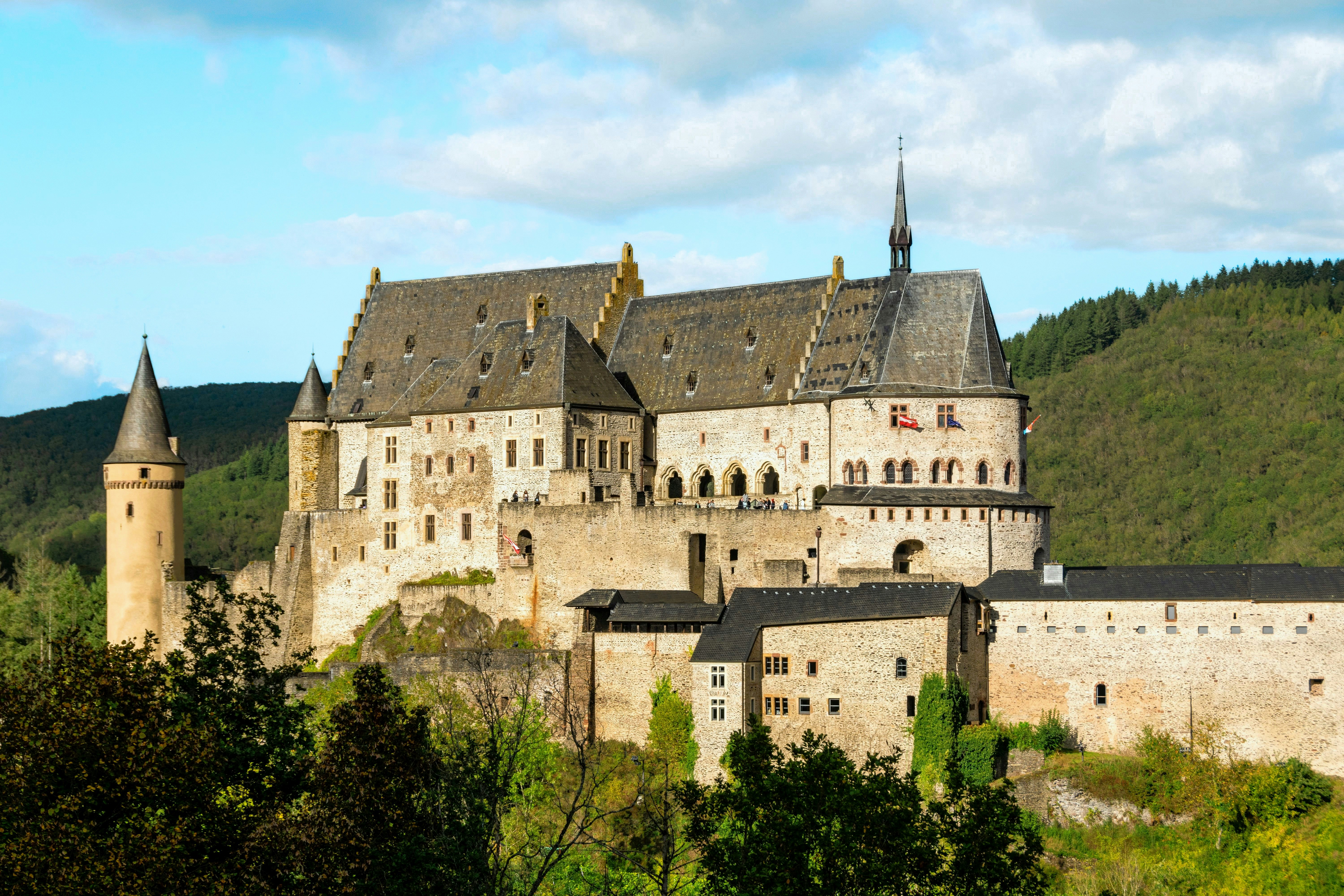 Historic castle with spires nestled in green hills.