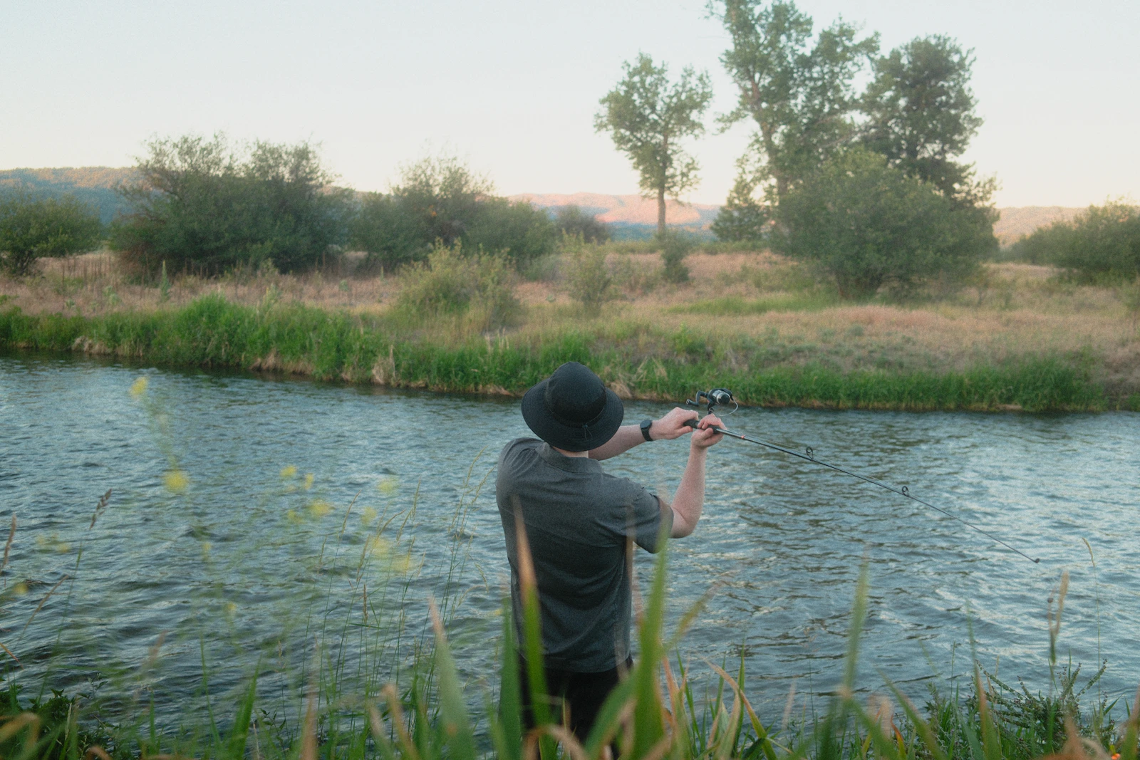 Angler casting a fishing rod into a river at dawn