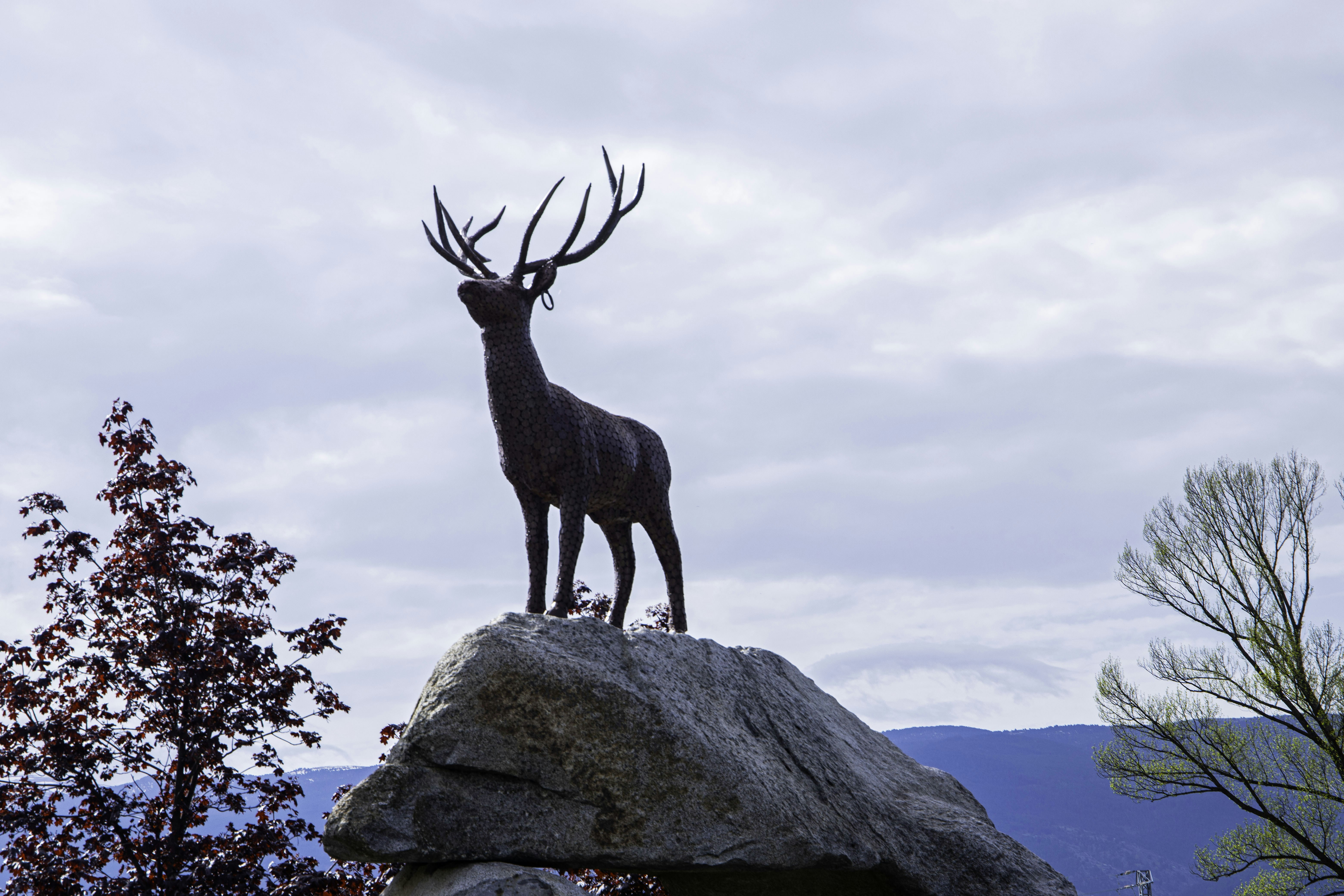 Deer statue on a rock against a cloudy sky.