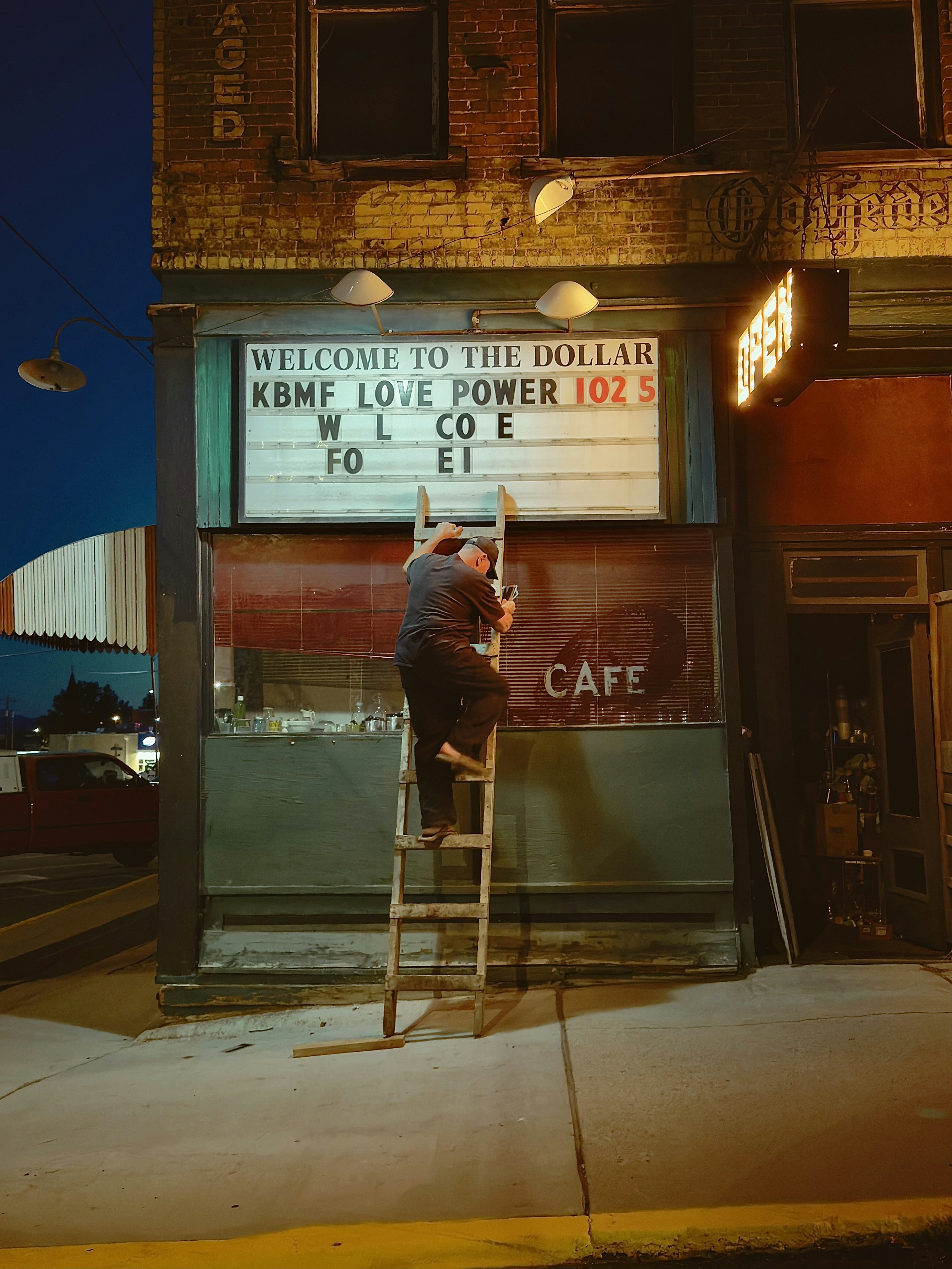 Man on ladder changing letters on an illuminated storefront sign.