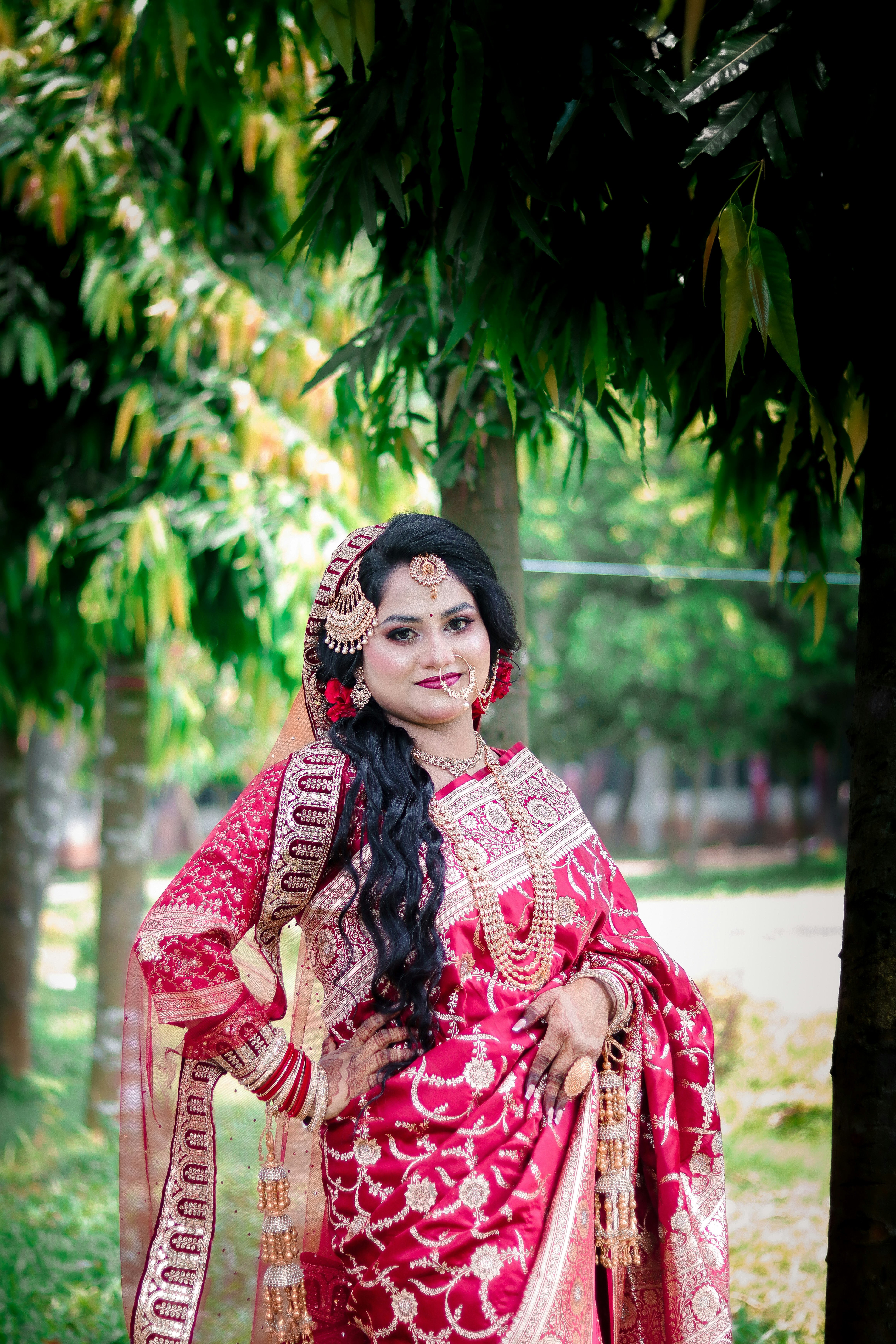 A woman in a beautiful red traditional outfit poses outdoors.