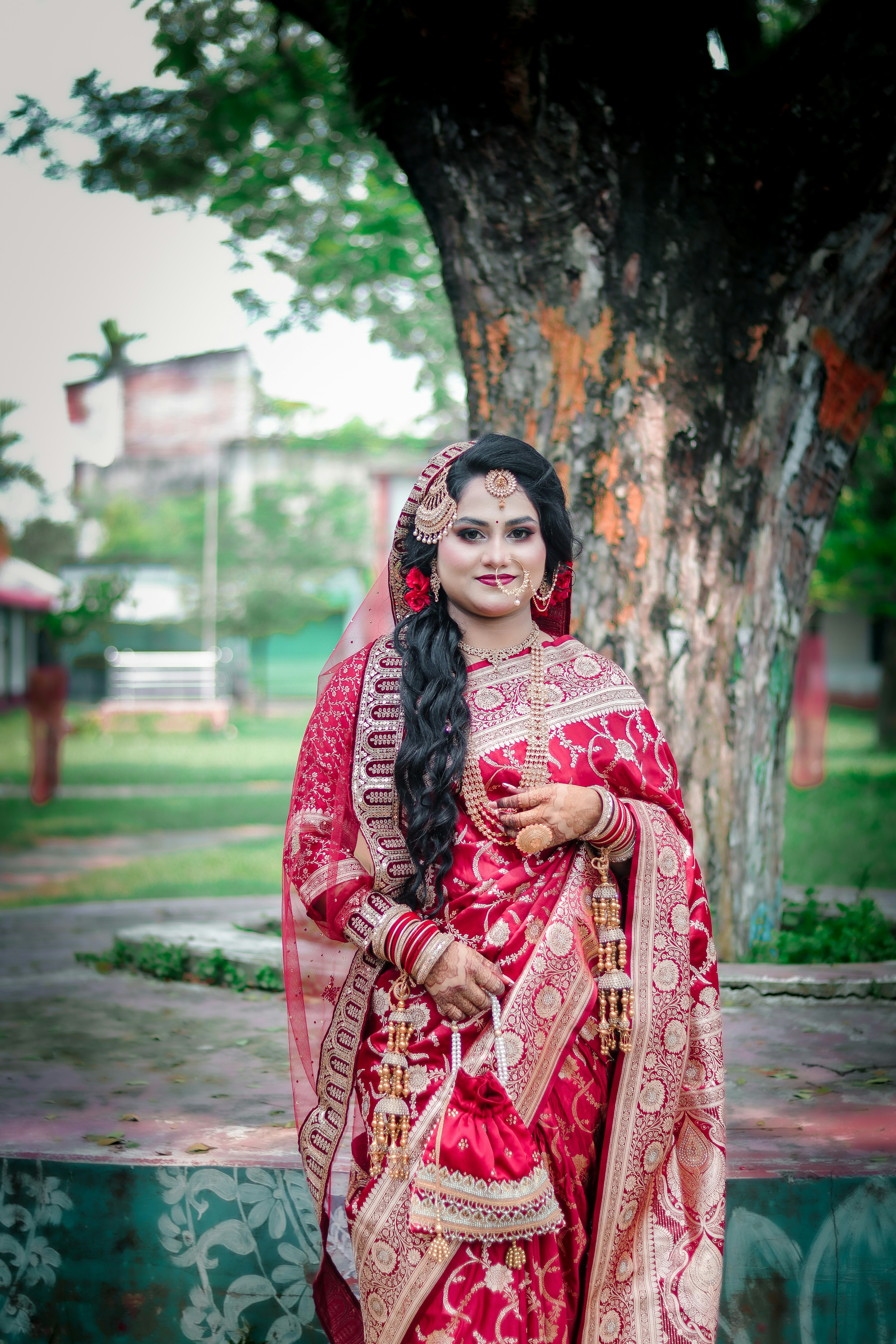 Beautiful bride in red and gold traditional attire outdoors.