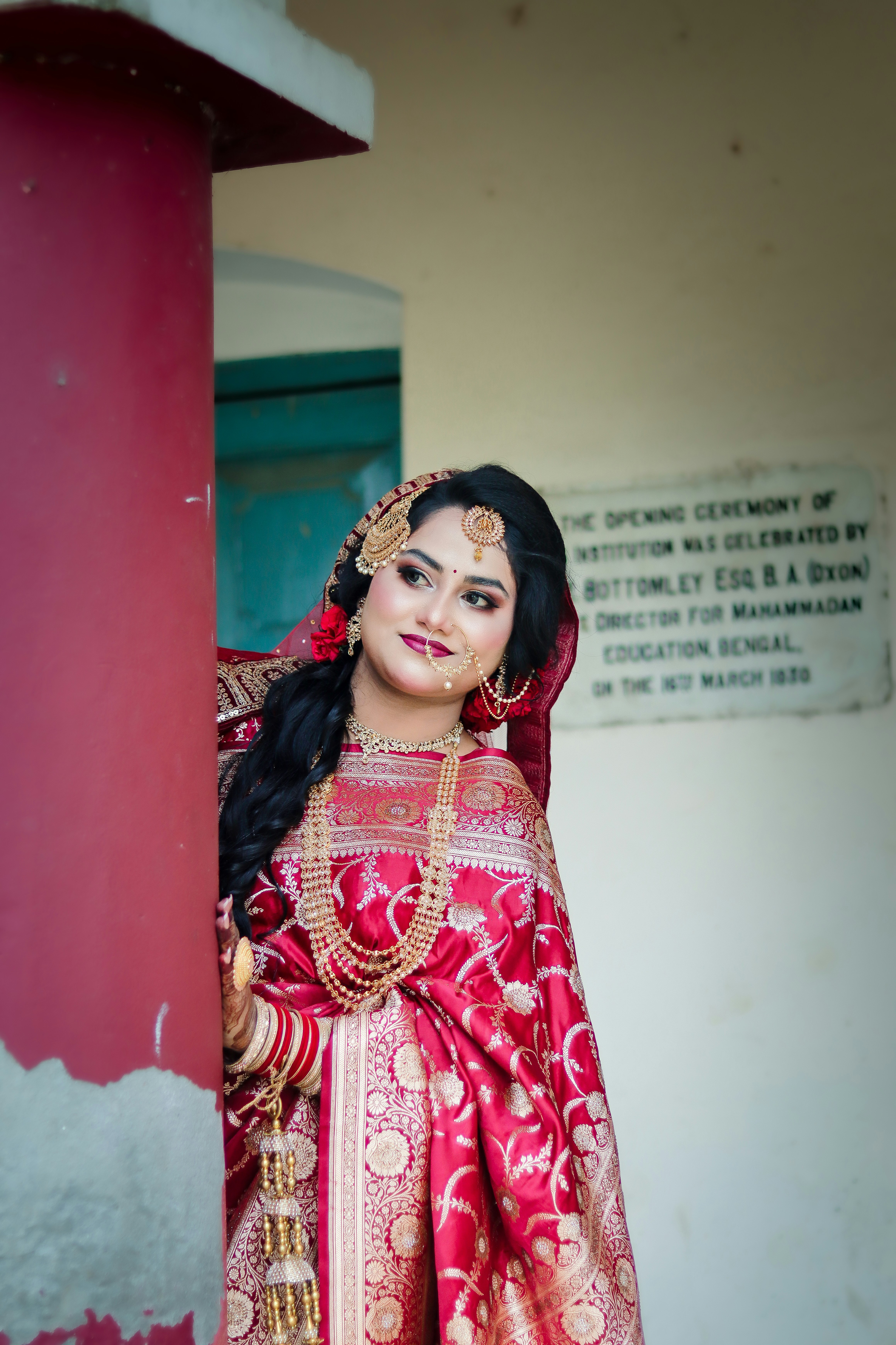 Smiling woman in traditional red saree with intricate gold jewelry.