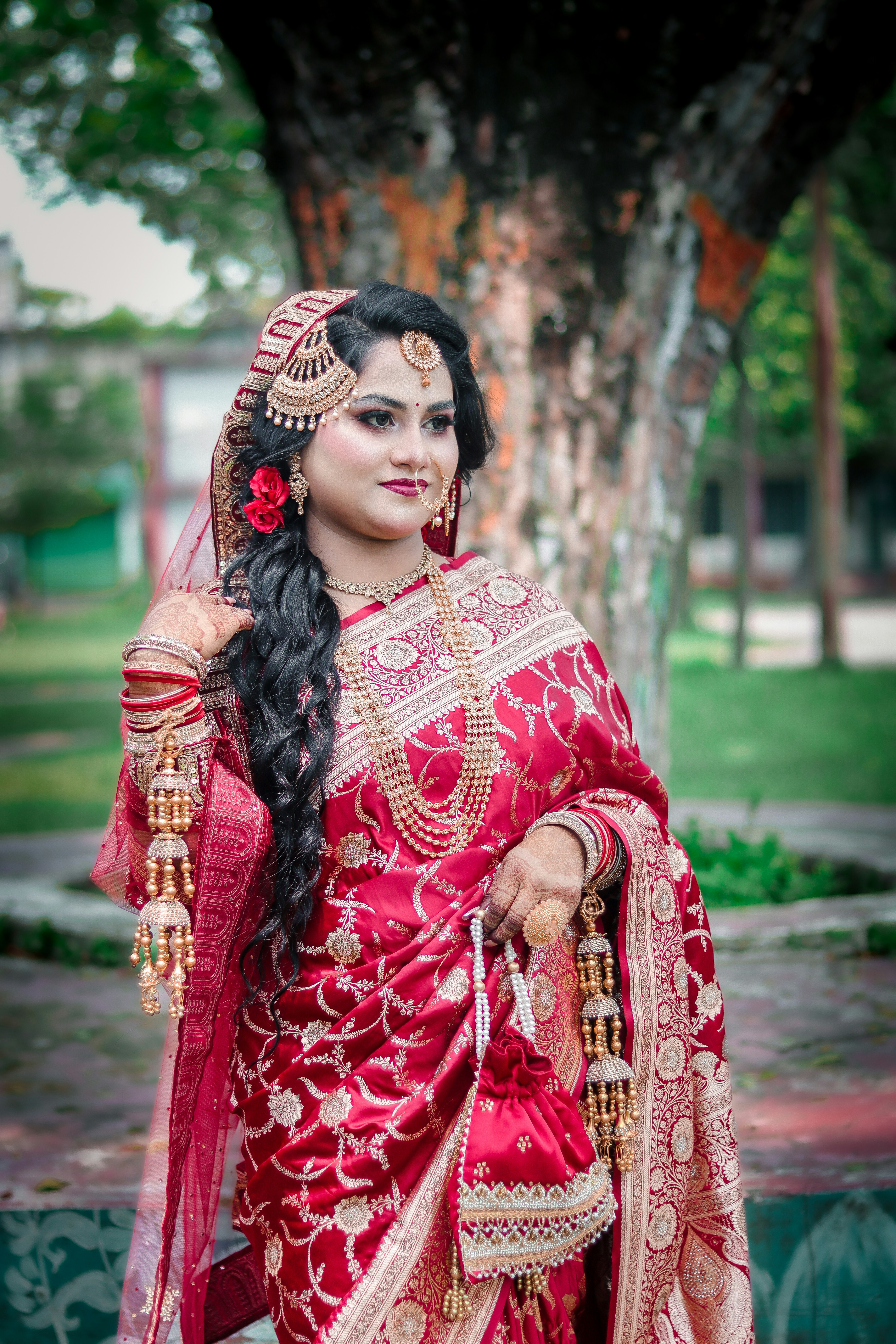 Woman in traditional red sari and gold jewelry outdoors.