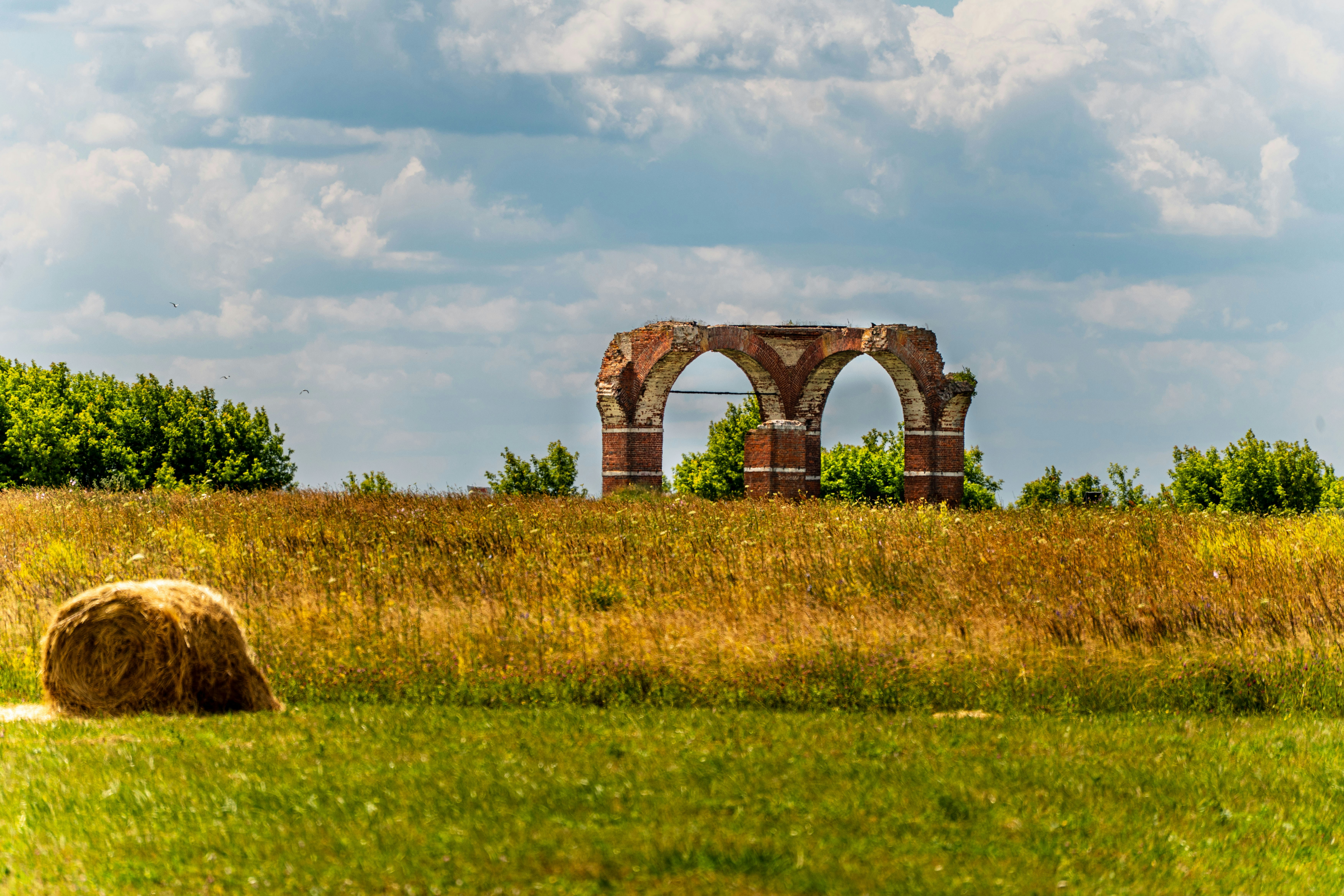 Hay bale in a field with ancient arch ruins.
