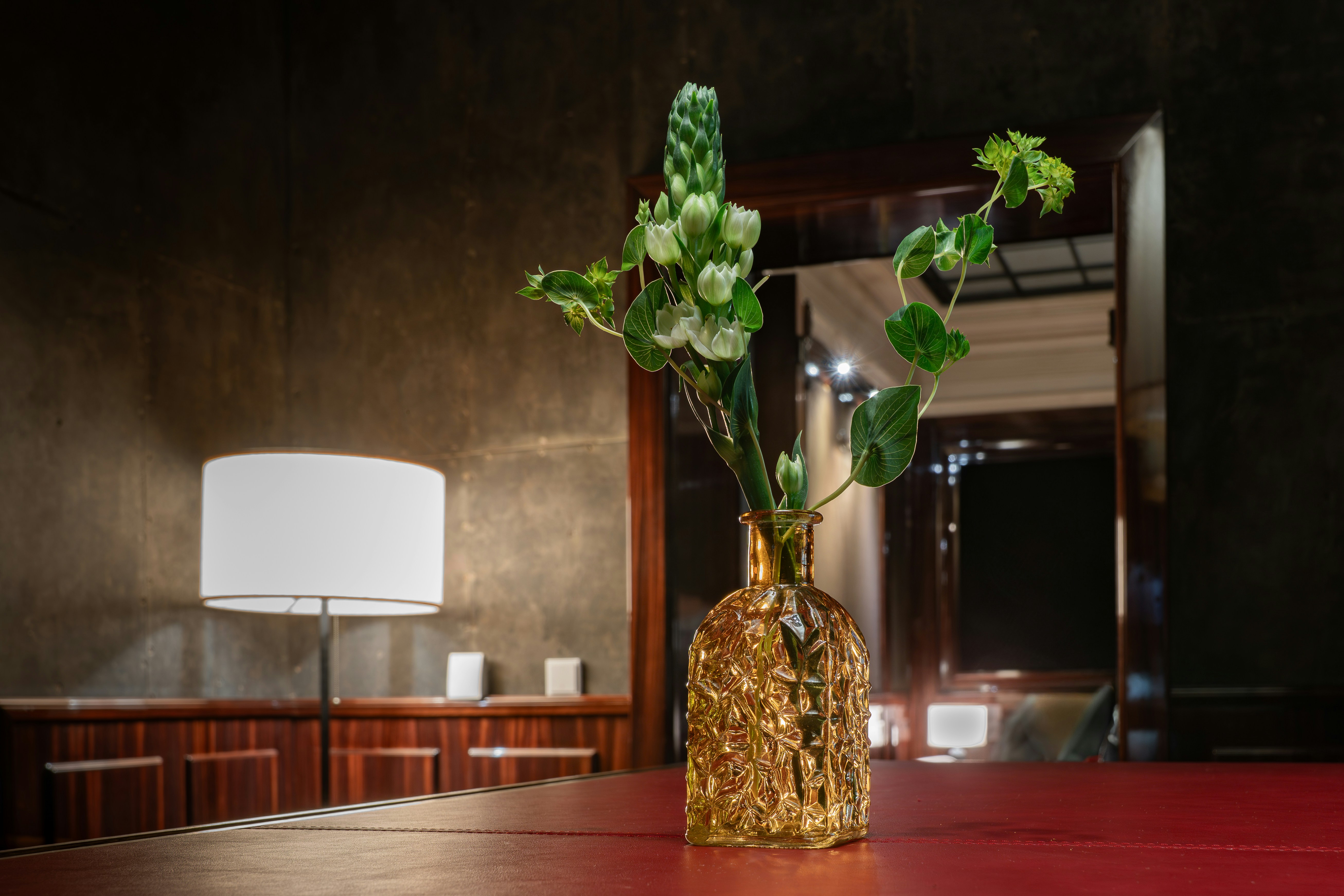 A golden vase with green plants on a red table.