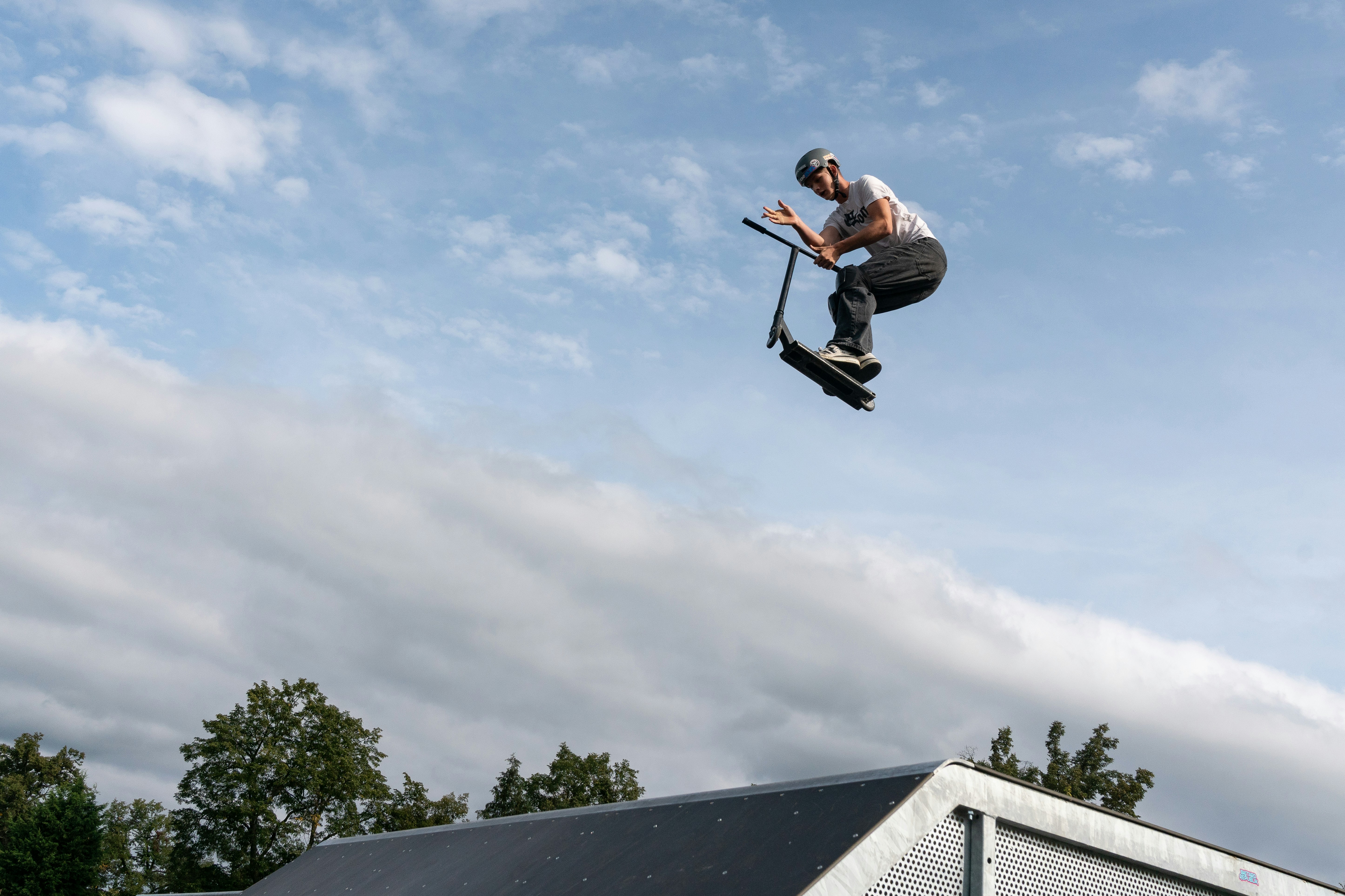 Scooter rider in mid-air performing trick against cloudy sky.