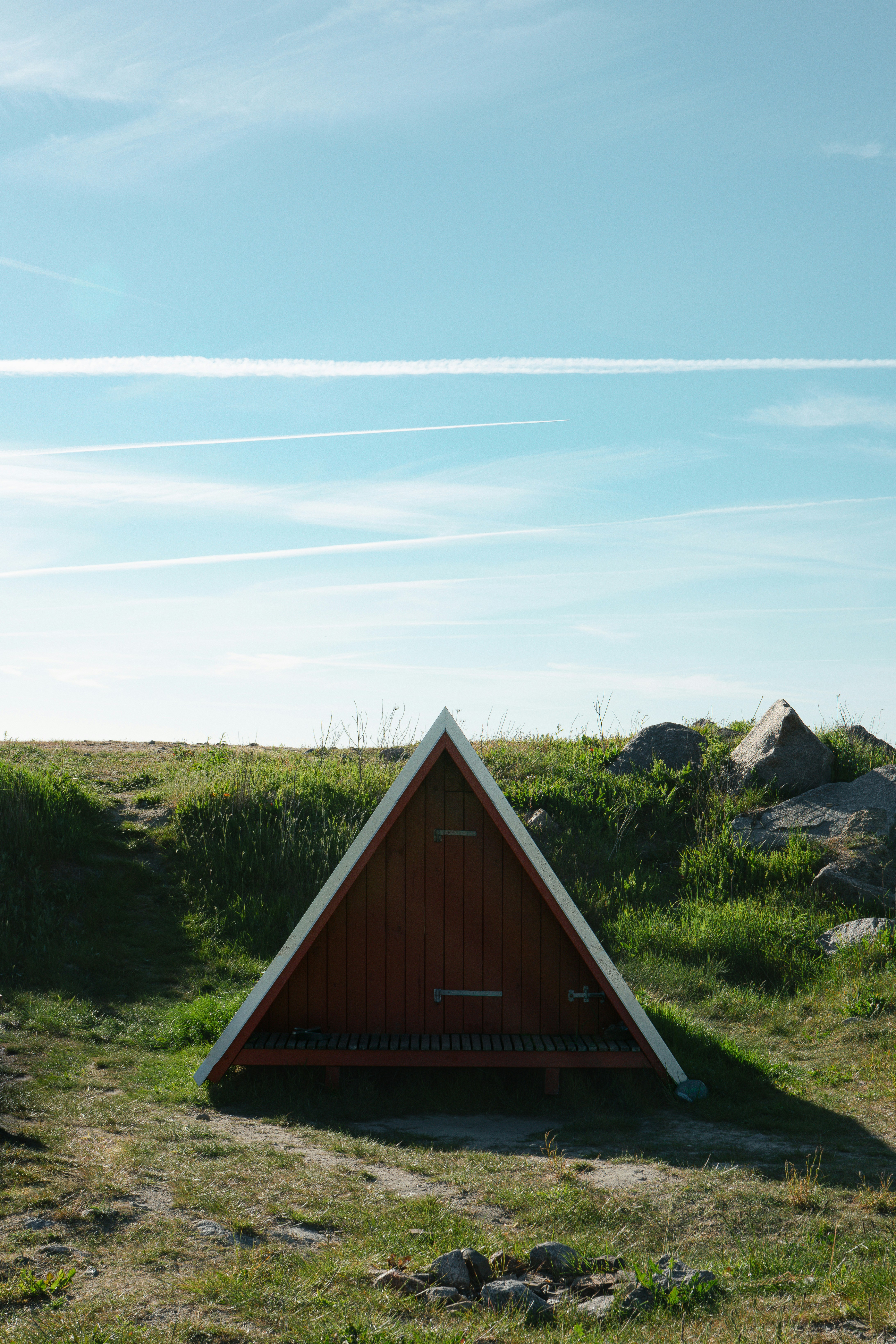 Refugio triangular rojo en un campo de hierba bajo un cielo azul.