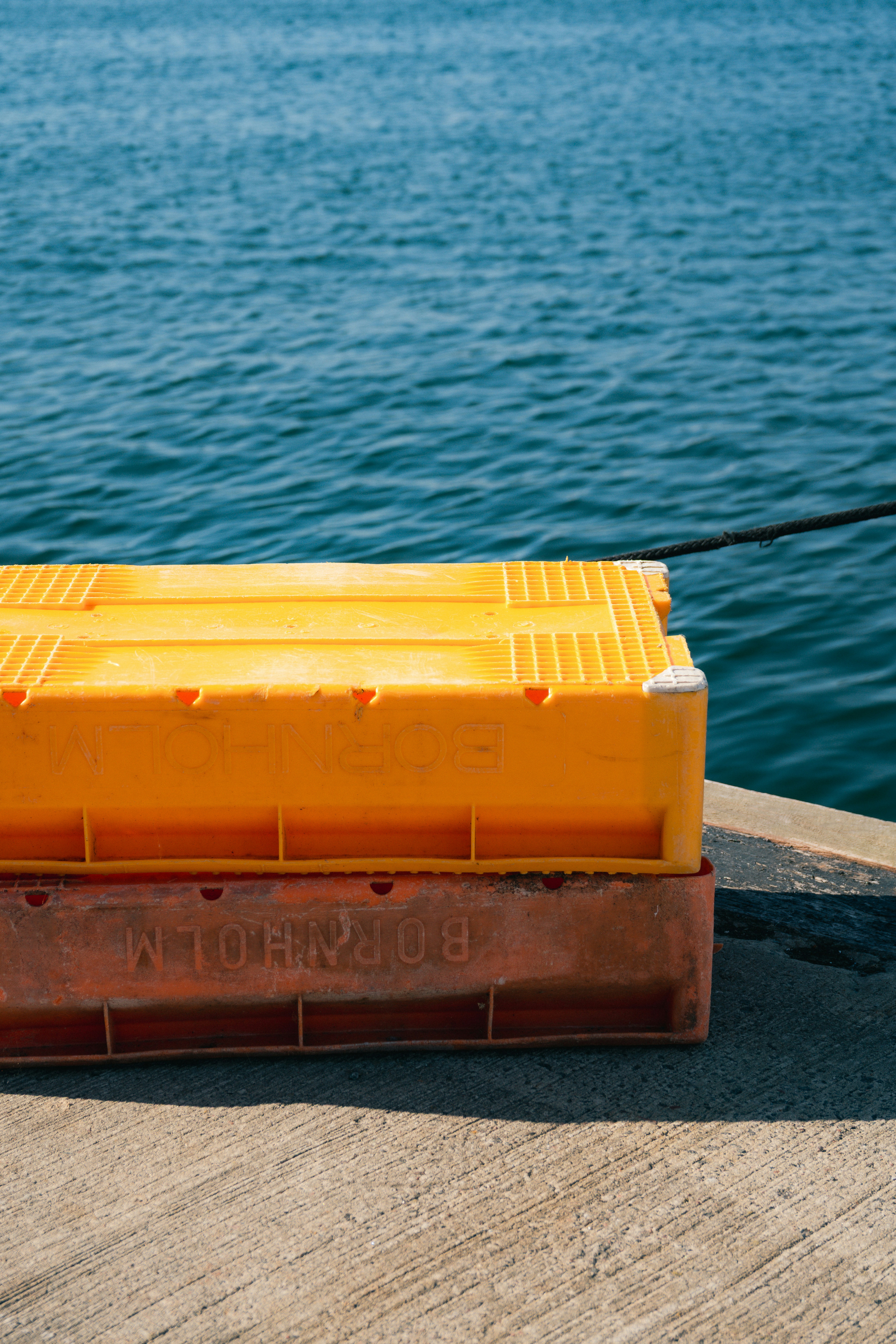Una caja amarillo-anaranjada en un muelle junto a aguas azules.
