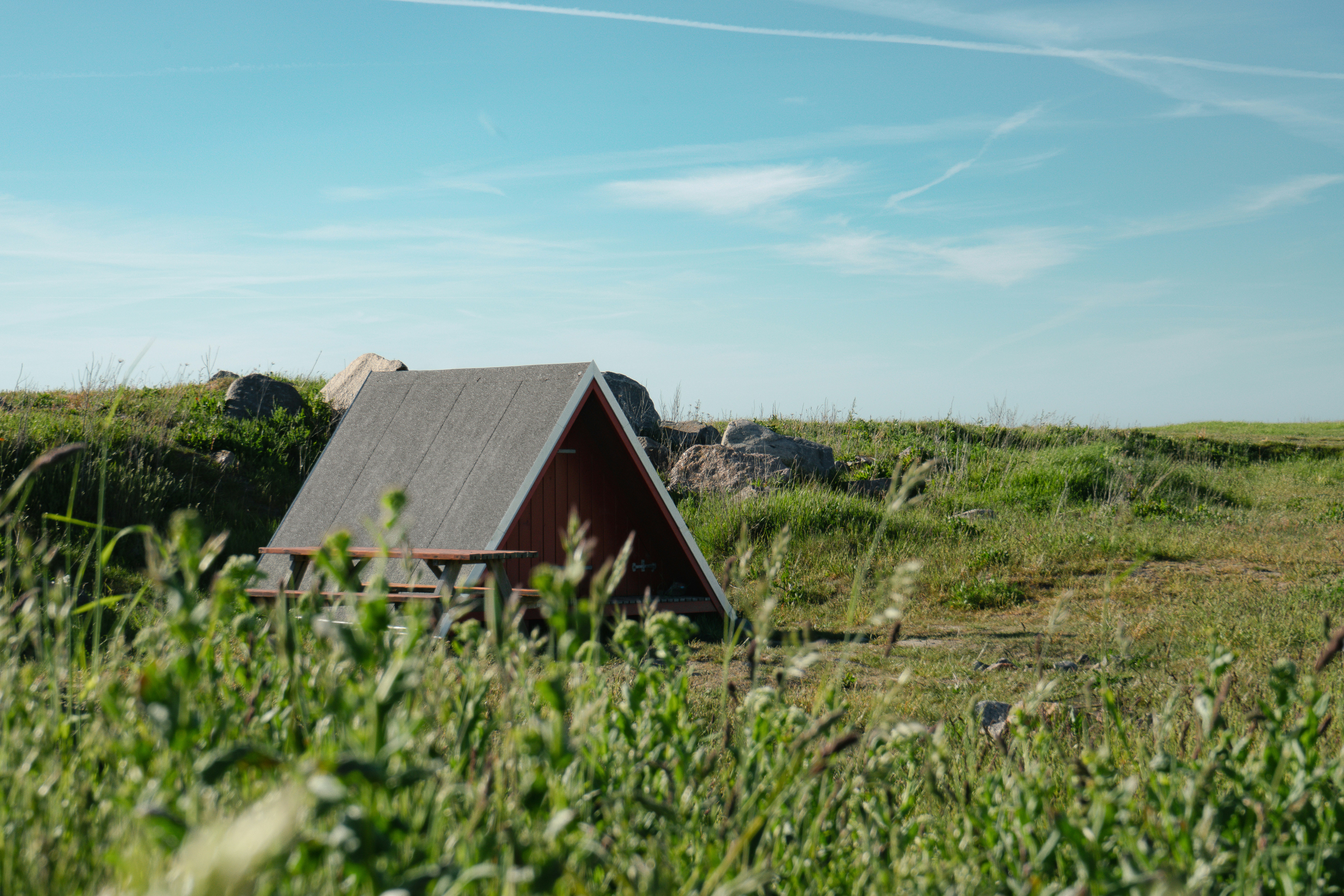 Un refugio en forma de A en un campo de hierba bajo un cielo azul.