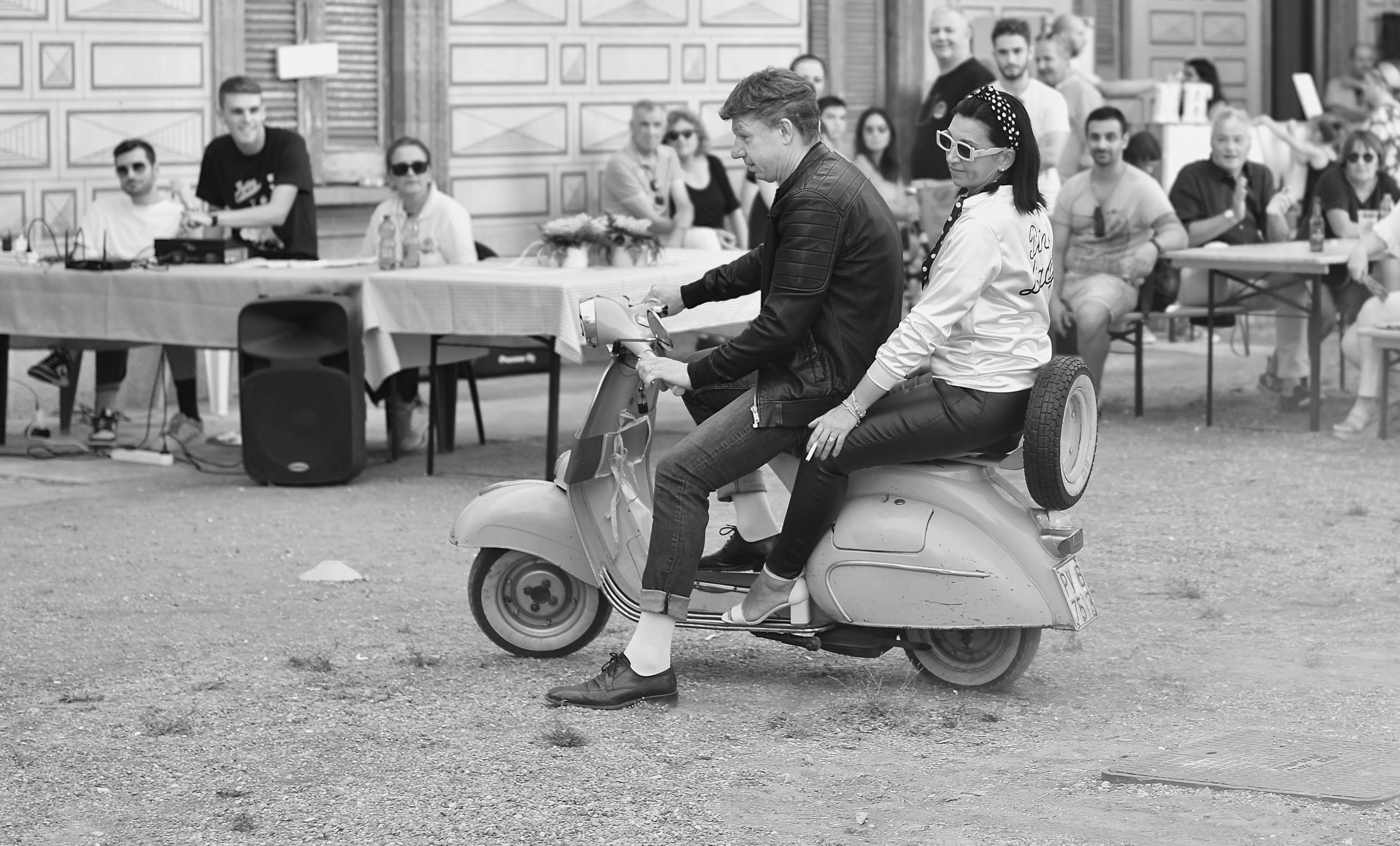 Man and woman on a vintage scooter during an event.