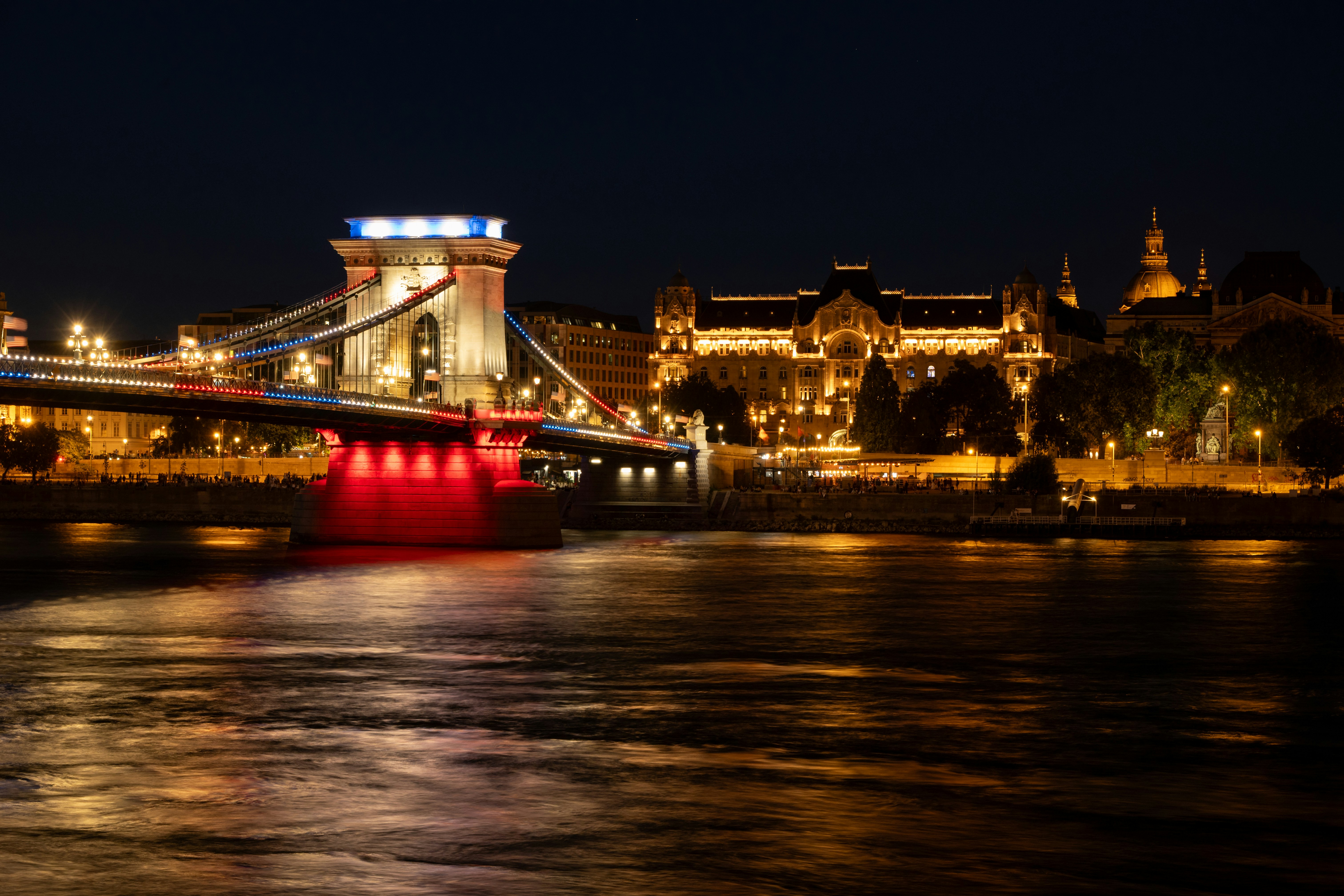 Pont illuminé et paysage urbain reflétés sur la rivière la nuit.