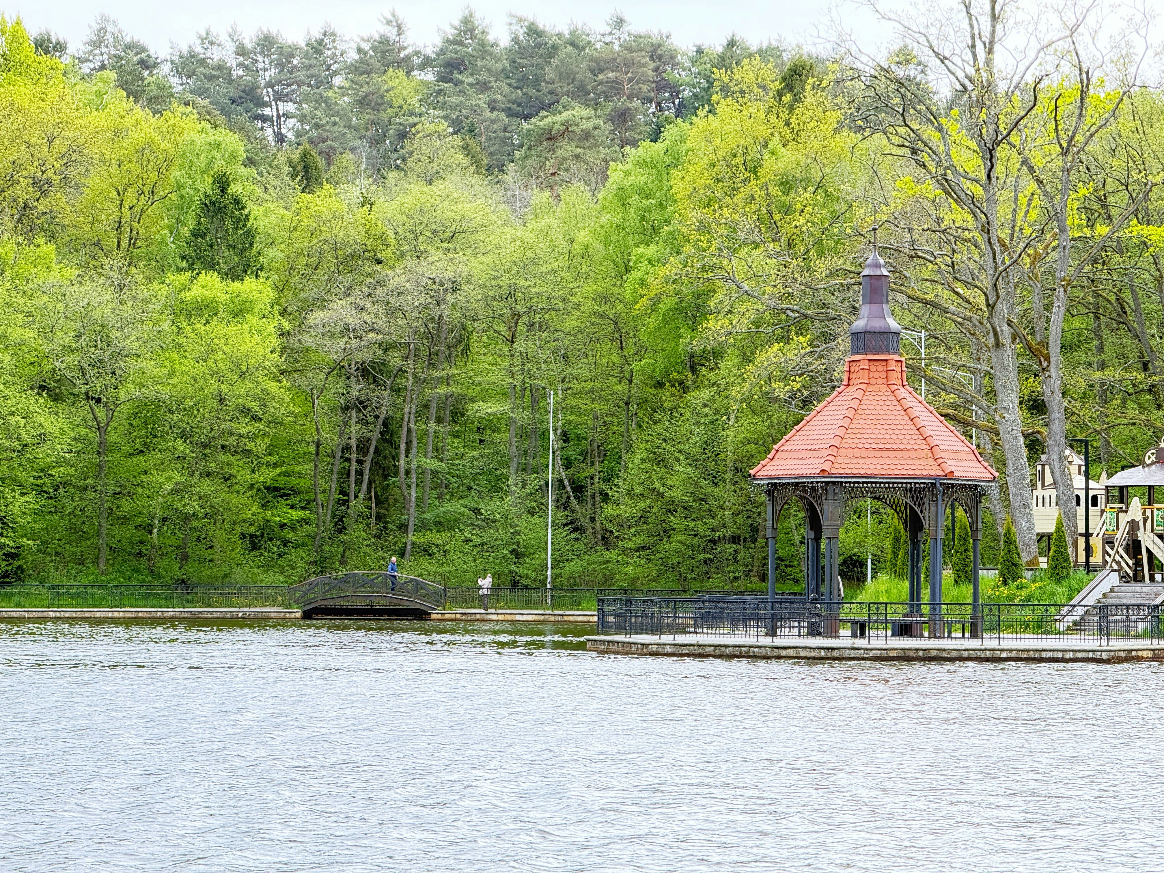 Serene lake with a gazebo and lush green trees.