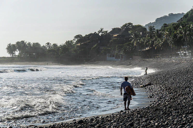 A surfer walking a rocky beach as waves break